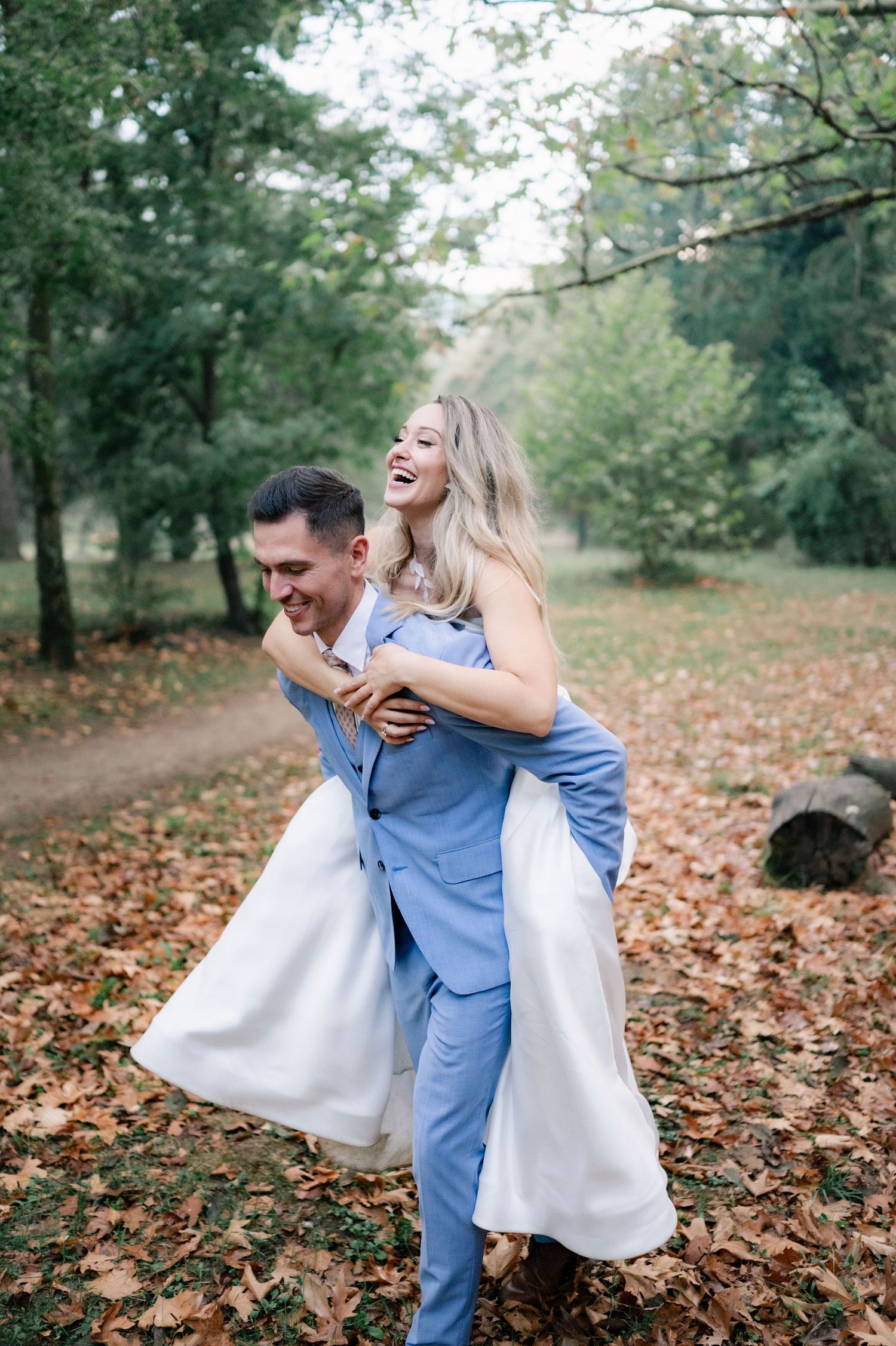 A couple shares joyful moments together in an autumn park setting with fallen leaves on the ground.