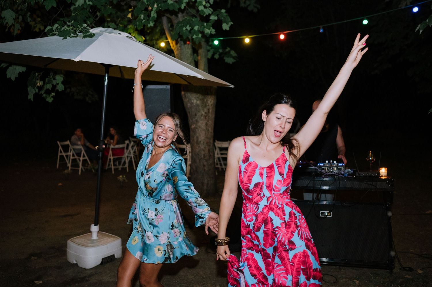 Two friends in colorful dresses dance and celebrate together at an outdoor nighttime party.
