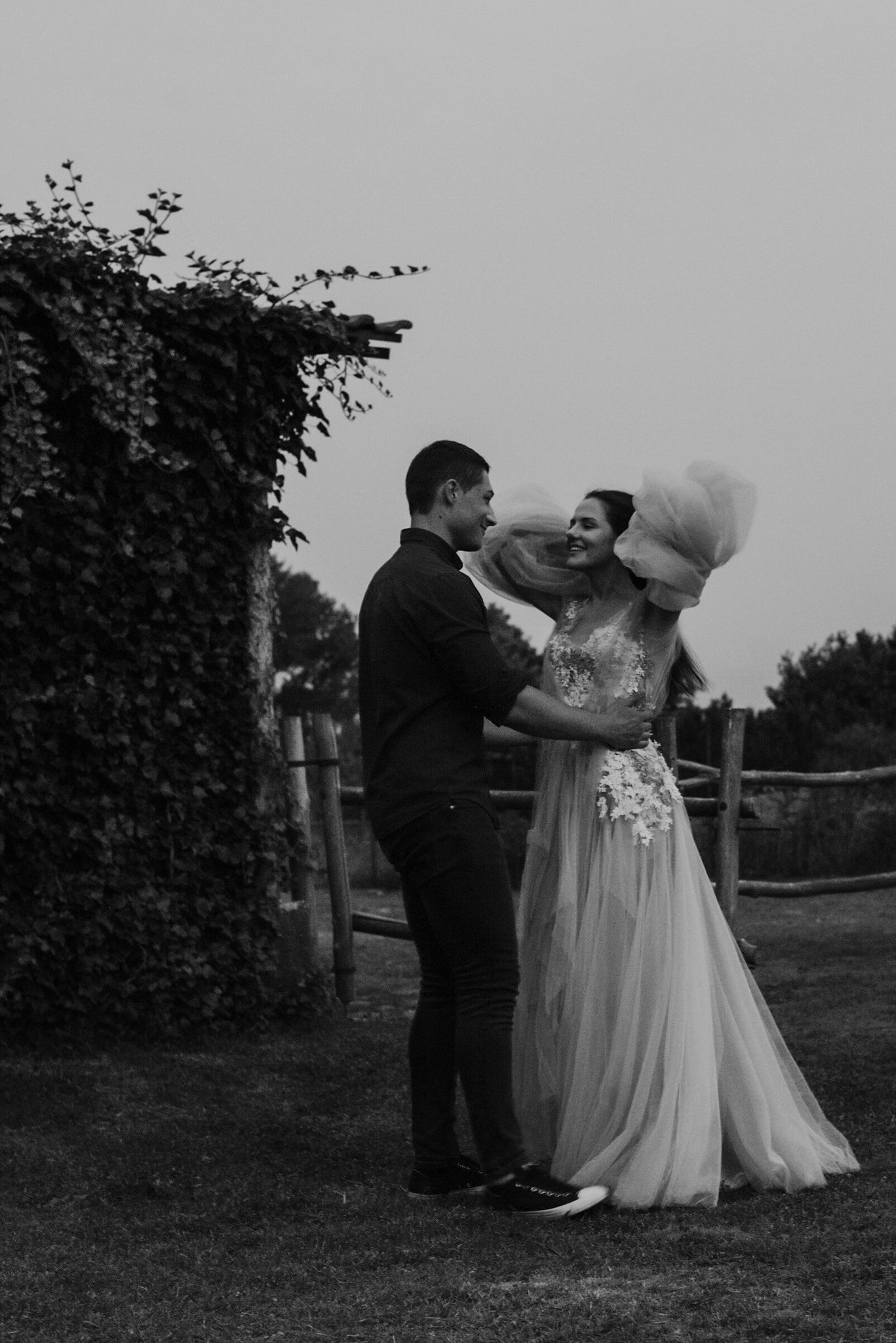 A couple shares an intimate moment in their wedding attire against a garden backdrop in black and white.