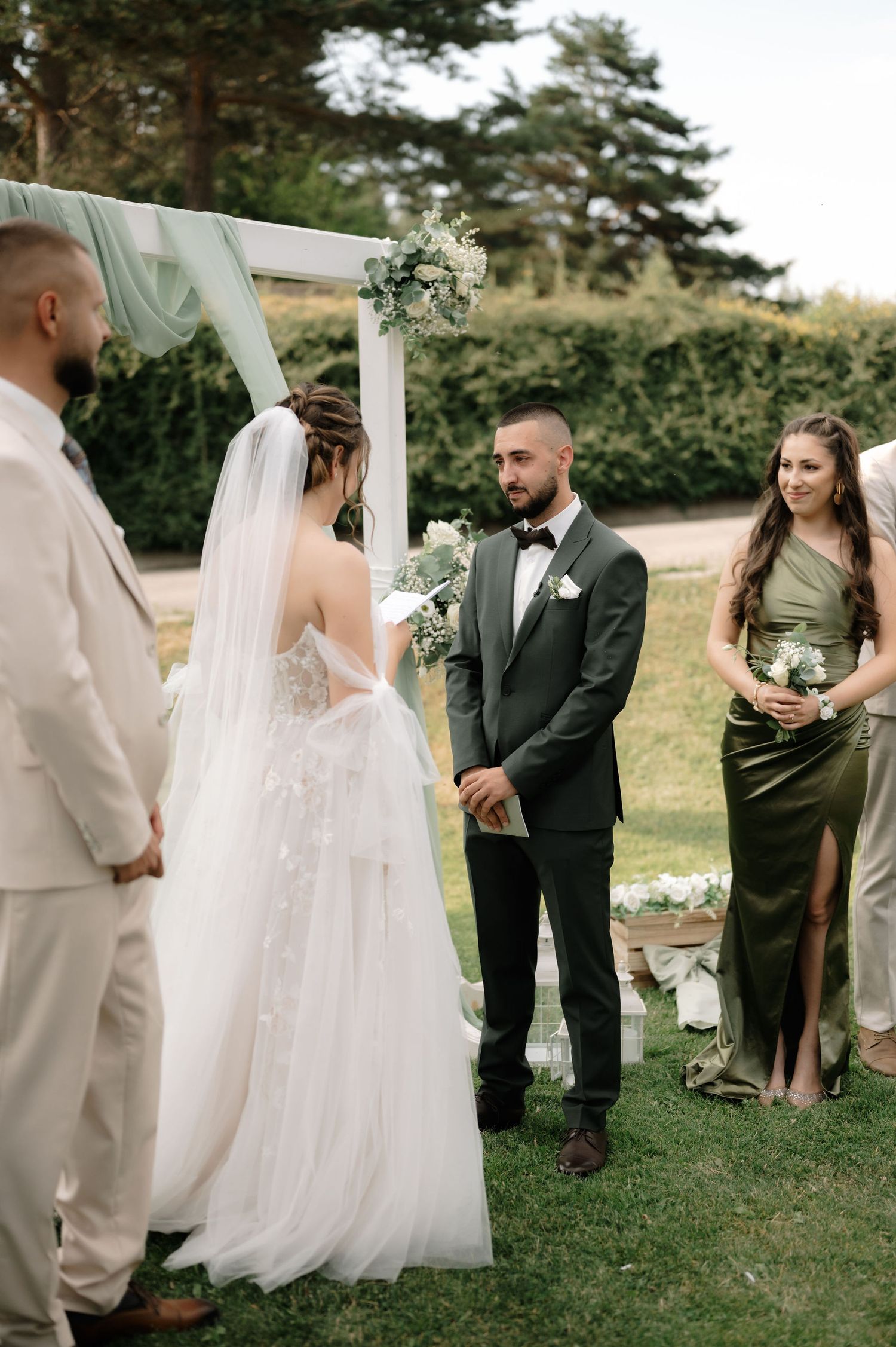 Wedding celebration on a grassy lawn with elegant white drapery and pine trees in the background.