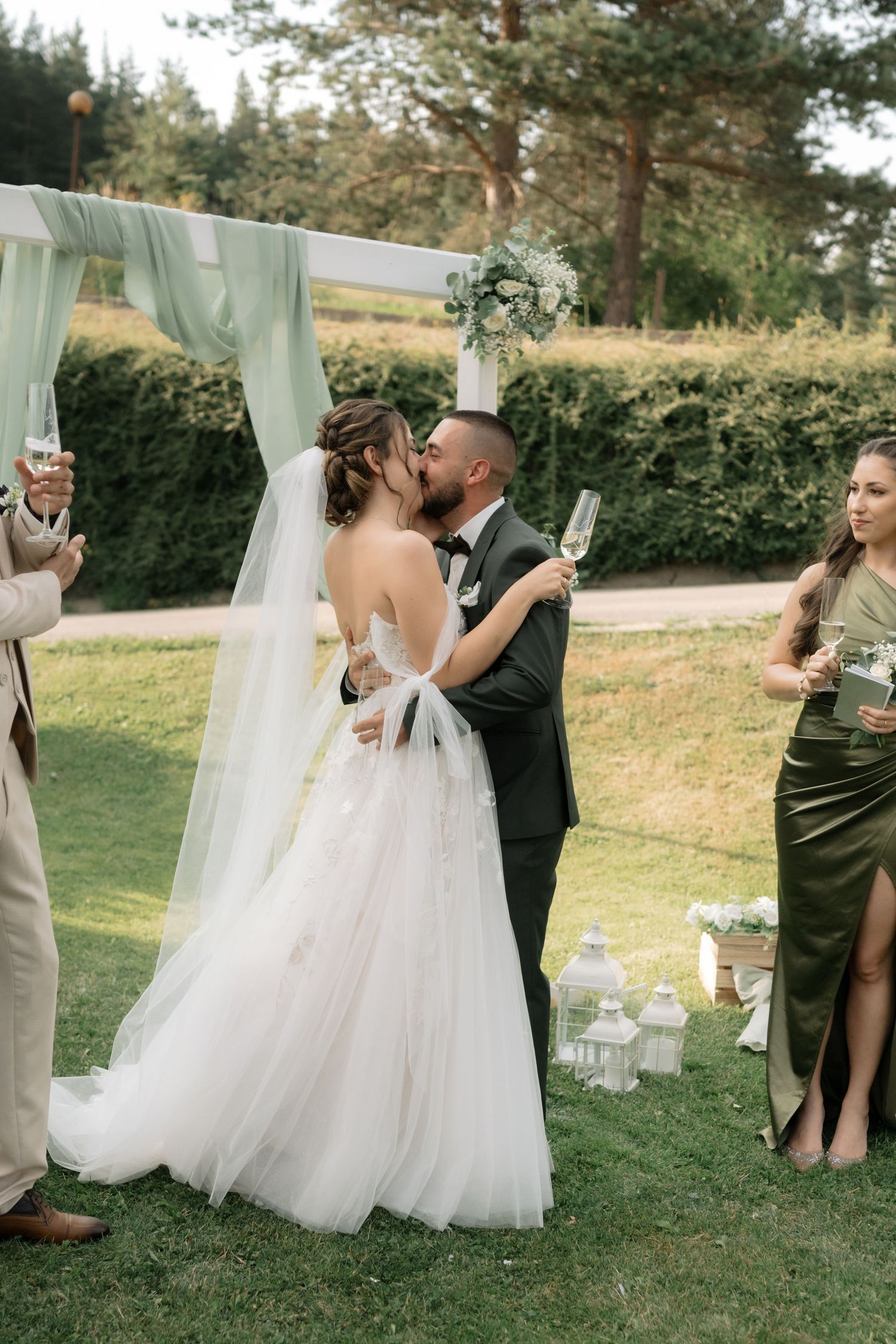 Wedding couple and guests toast with champagne glasses in an outdoor garden ceremony setting.
