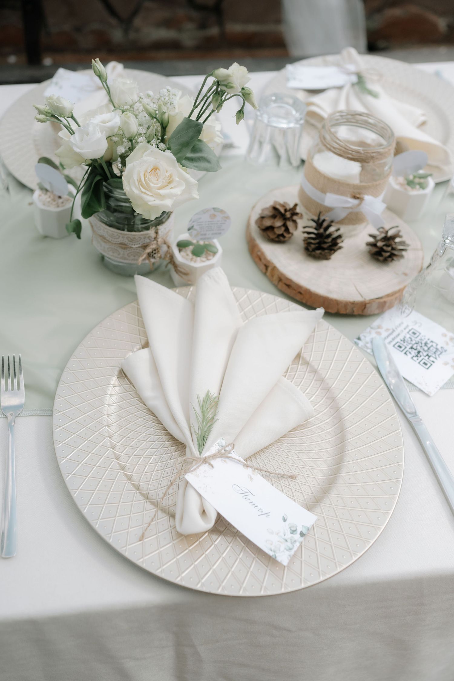 White place settings with pinecones and white roses create an elegant winter tablescape at a wedding reception.