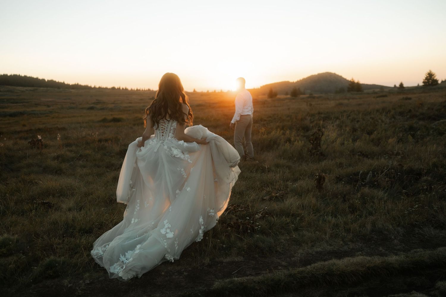 Silhouetted couple walking through field at sunset with dramatic lighting.