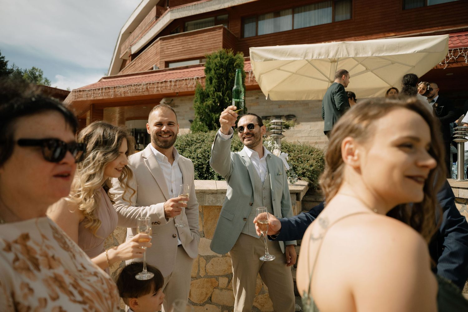 Guests celebrating outdoors at a wedding reception, raising glasses in a toast on a sunny patio.