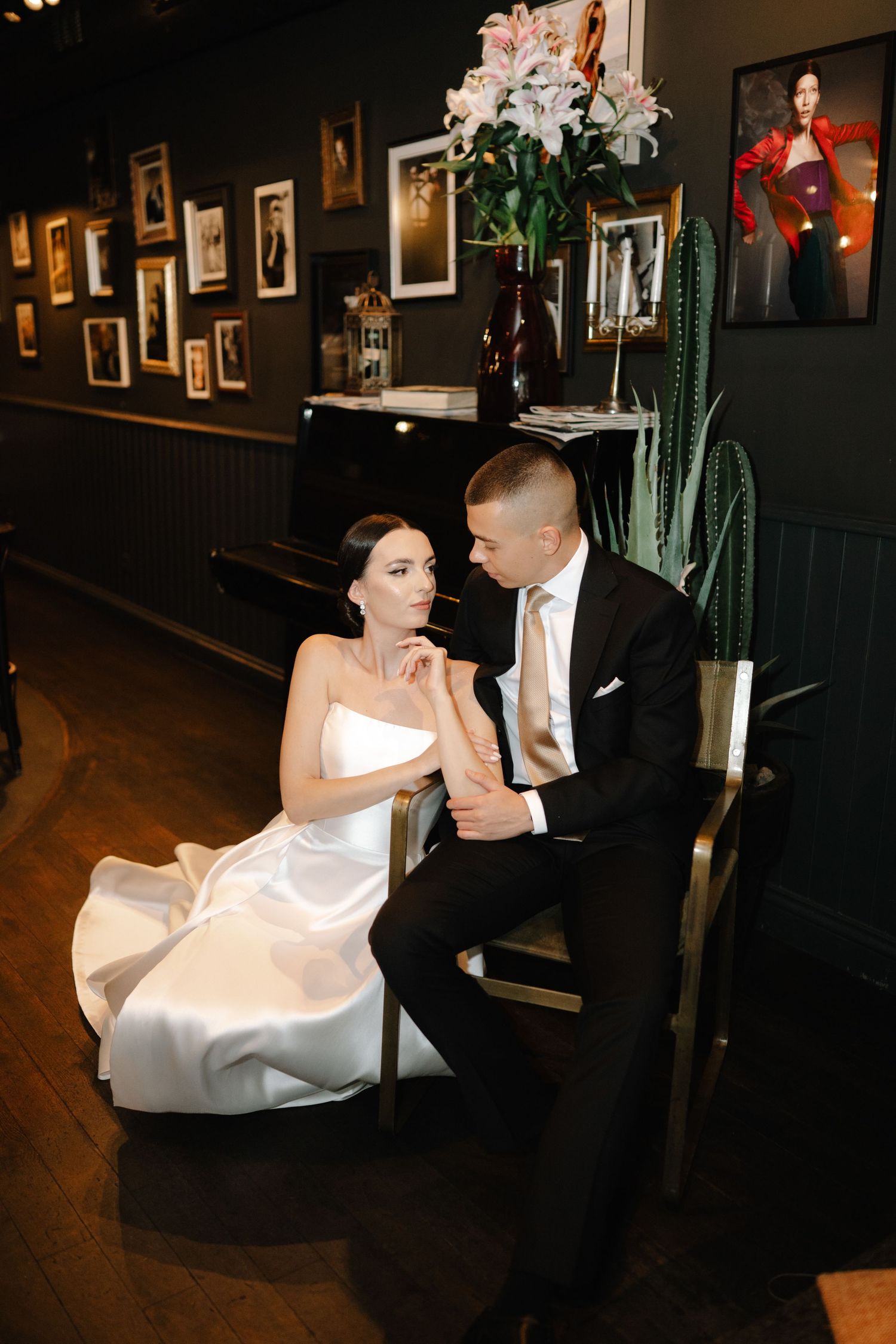 A couple shares an intimate moment in a dimly lit venue with dark walls adorned with framed photographs.