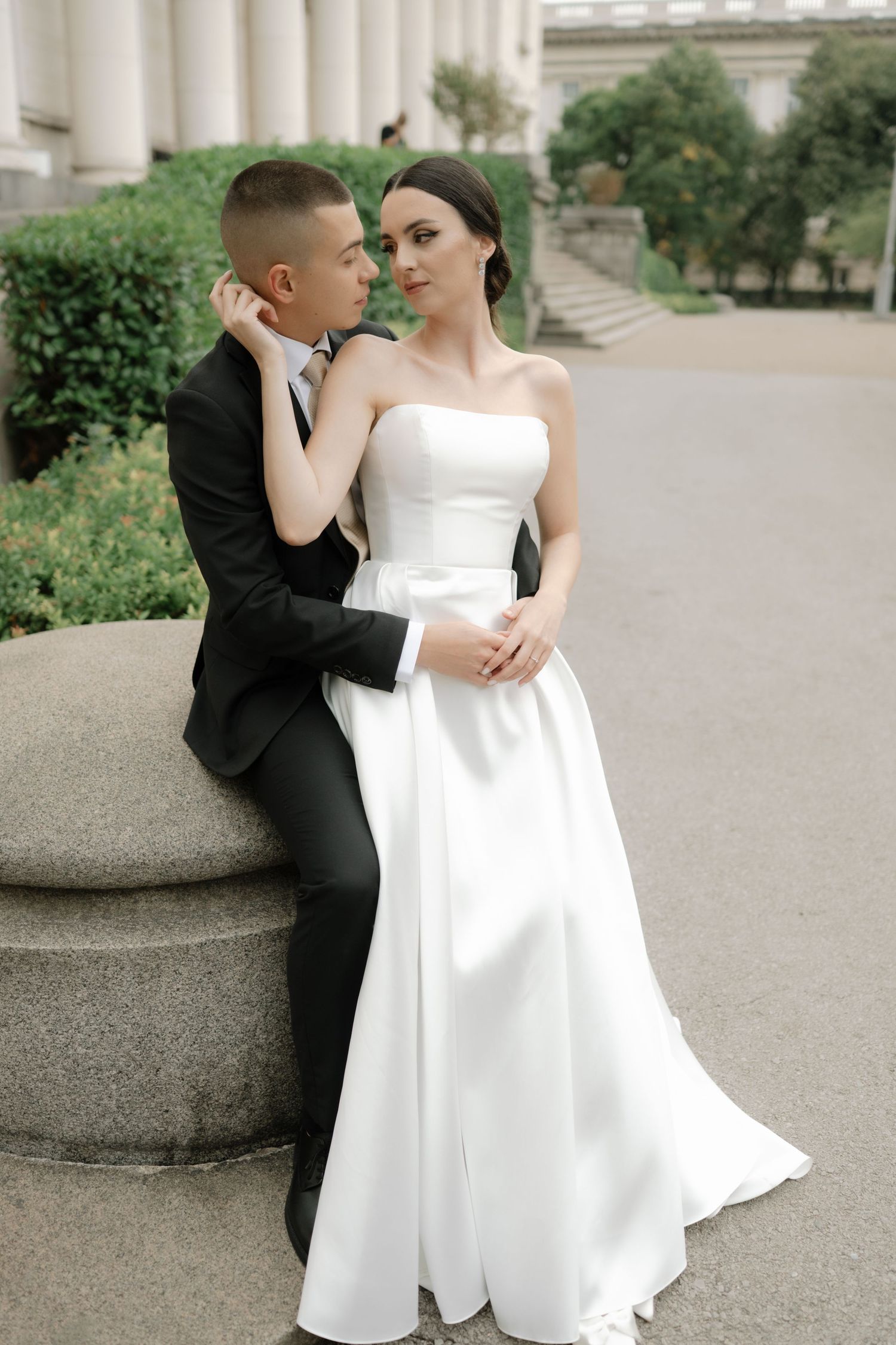 A couple in formal wedding attire share an intimate moment on stone steps during their outdoor photo session.