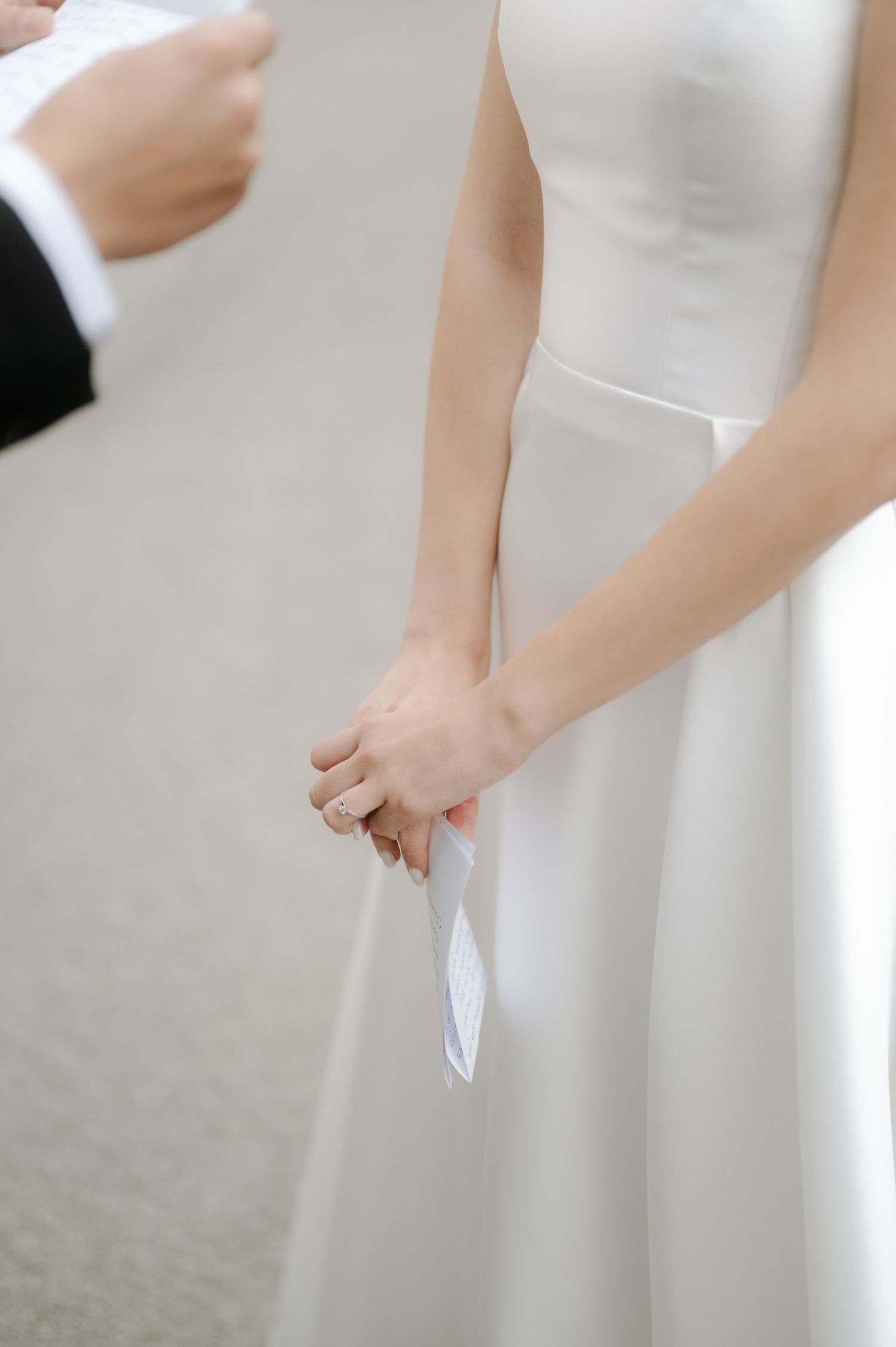 Close-up details of a white wedding dress showing elegant fabric and silhouette against a light background.