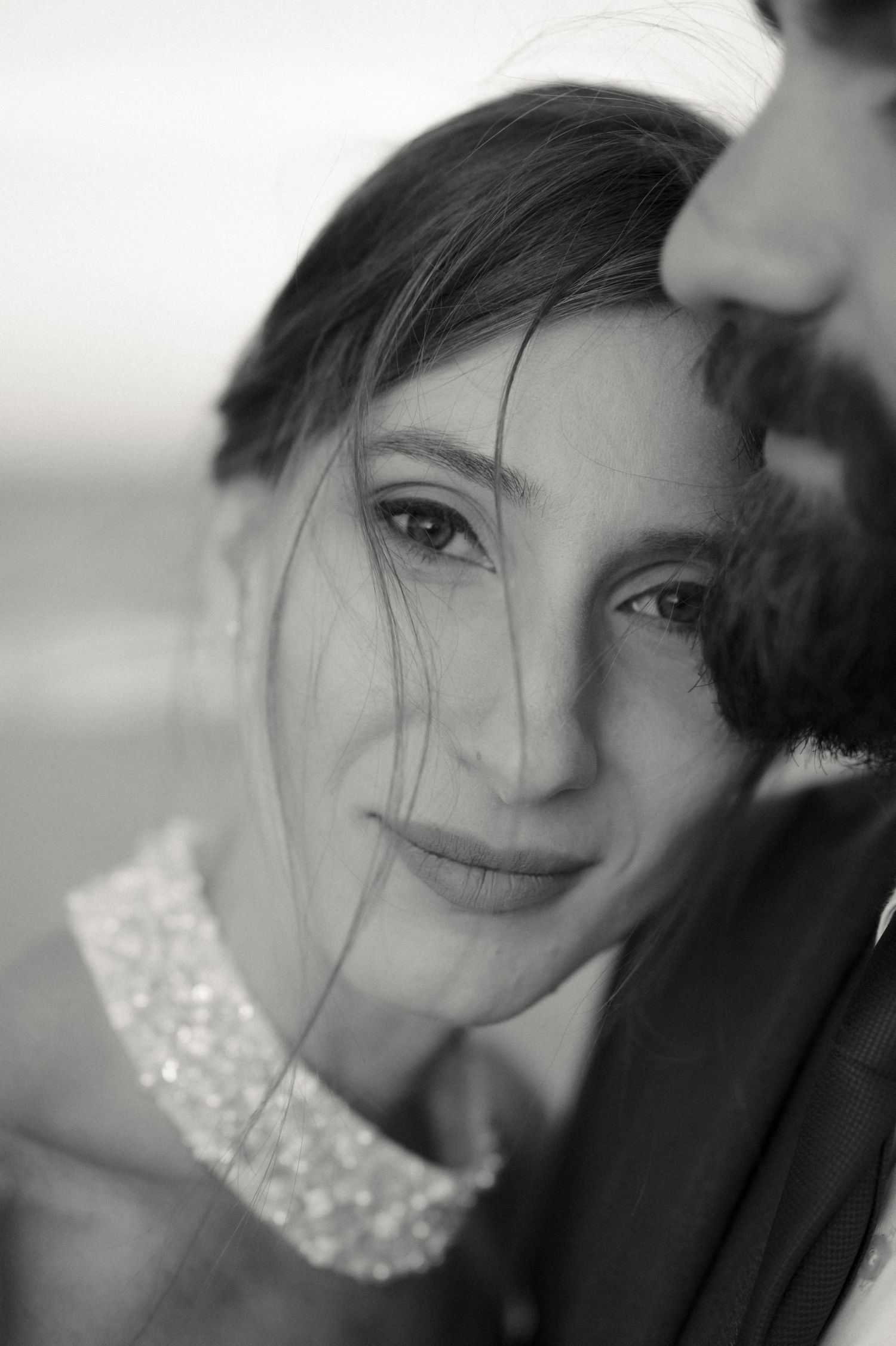 Black and white close-up portrait of a young woman smiling softly, hair blowing across her face.