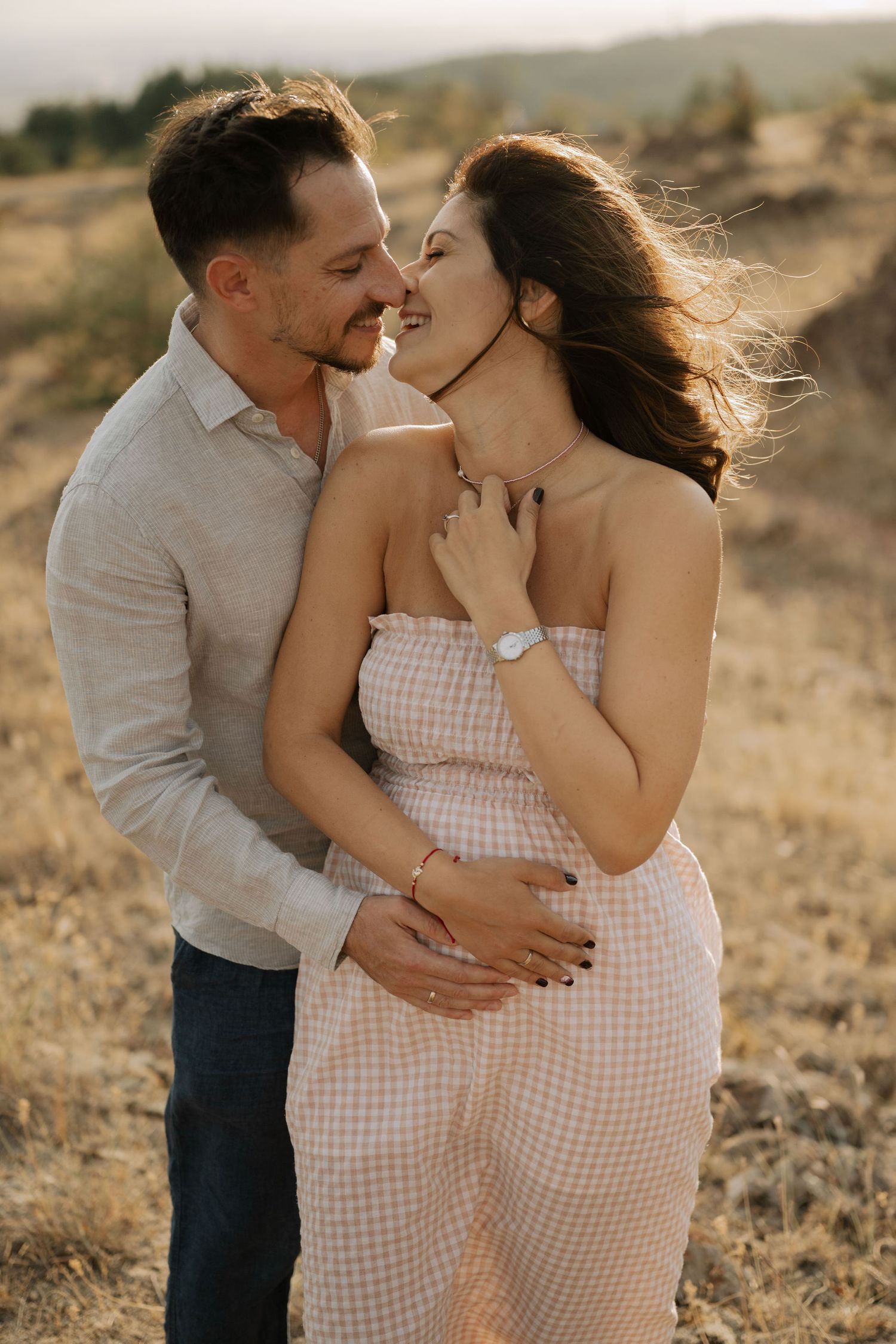 A couple embraces in a golden field during sunset as they share intimate moments in a maternity photoshoot.