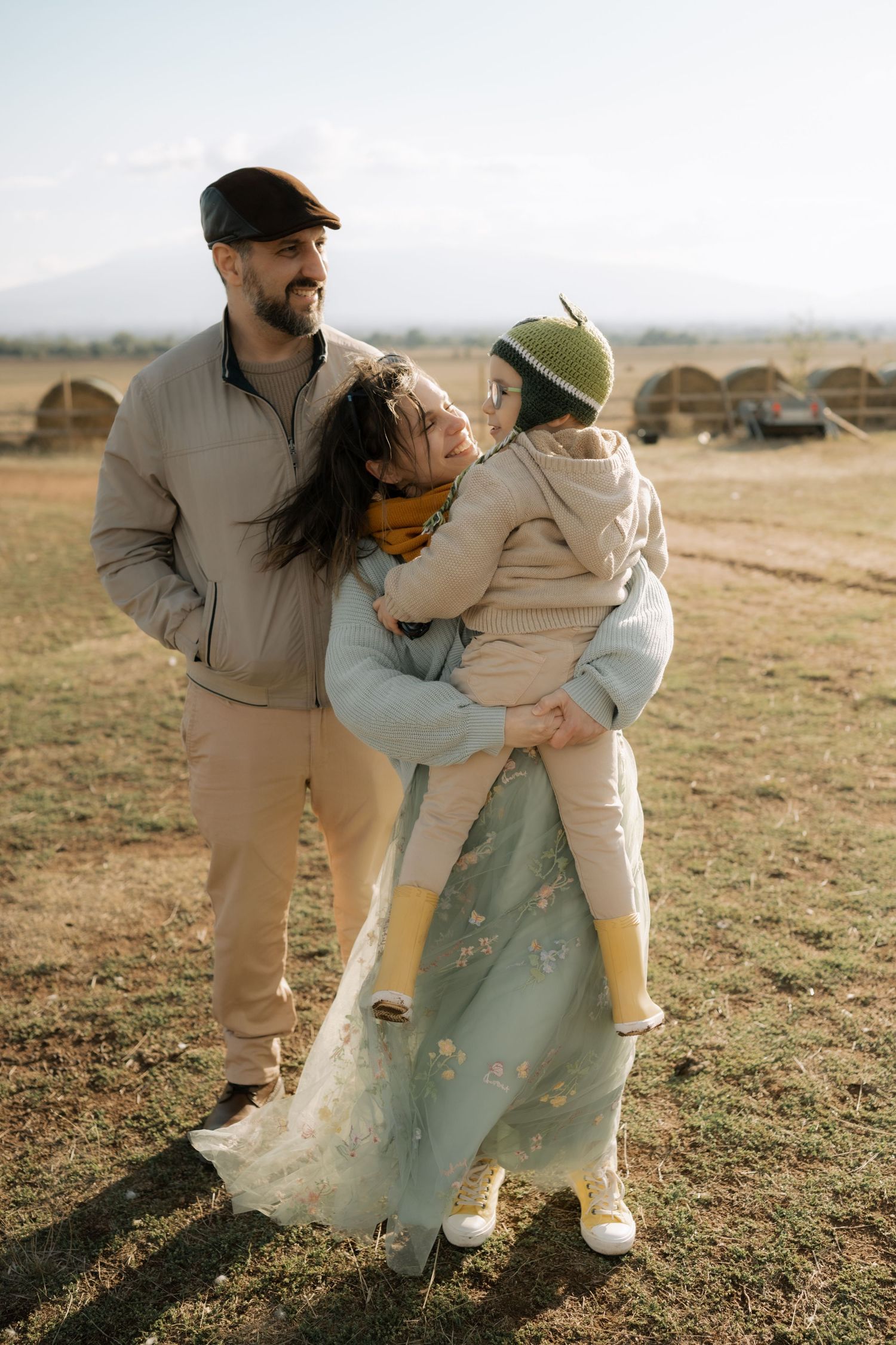 A family plays together in a grassy field during golden hour, creating a series of joyful candid moments.