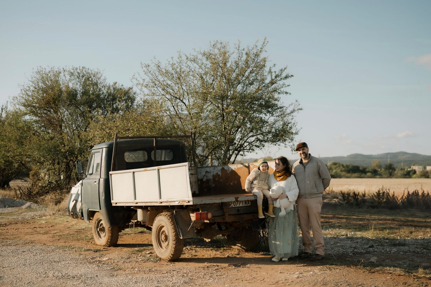 Vintage pickup truck parked in rural countryside with people gathered beside it at sunset.
