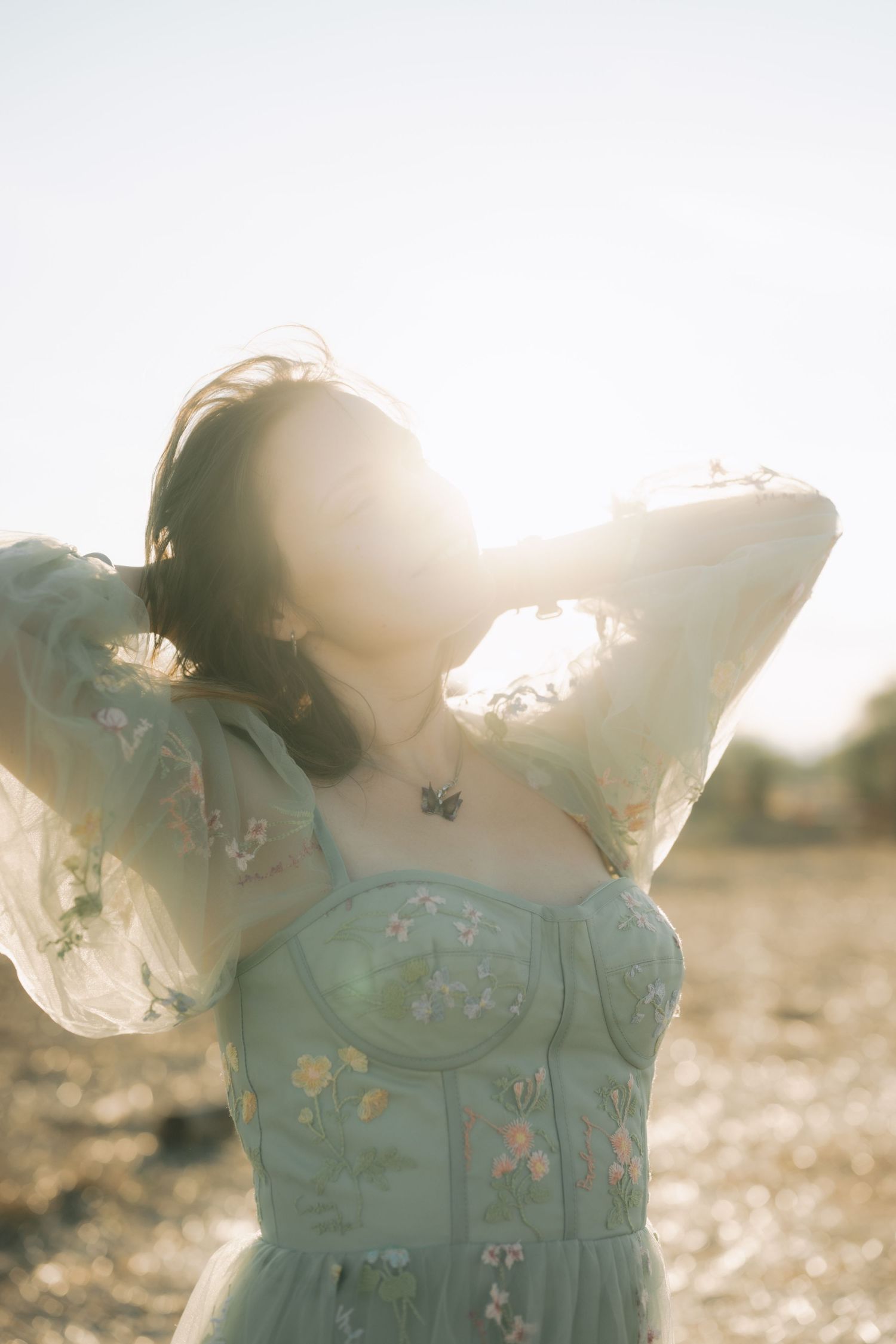 A person in a mint green floral dress stands in golden sunlight creating a dreamy, ethereal silhouette.