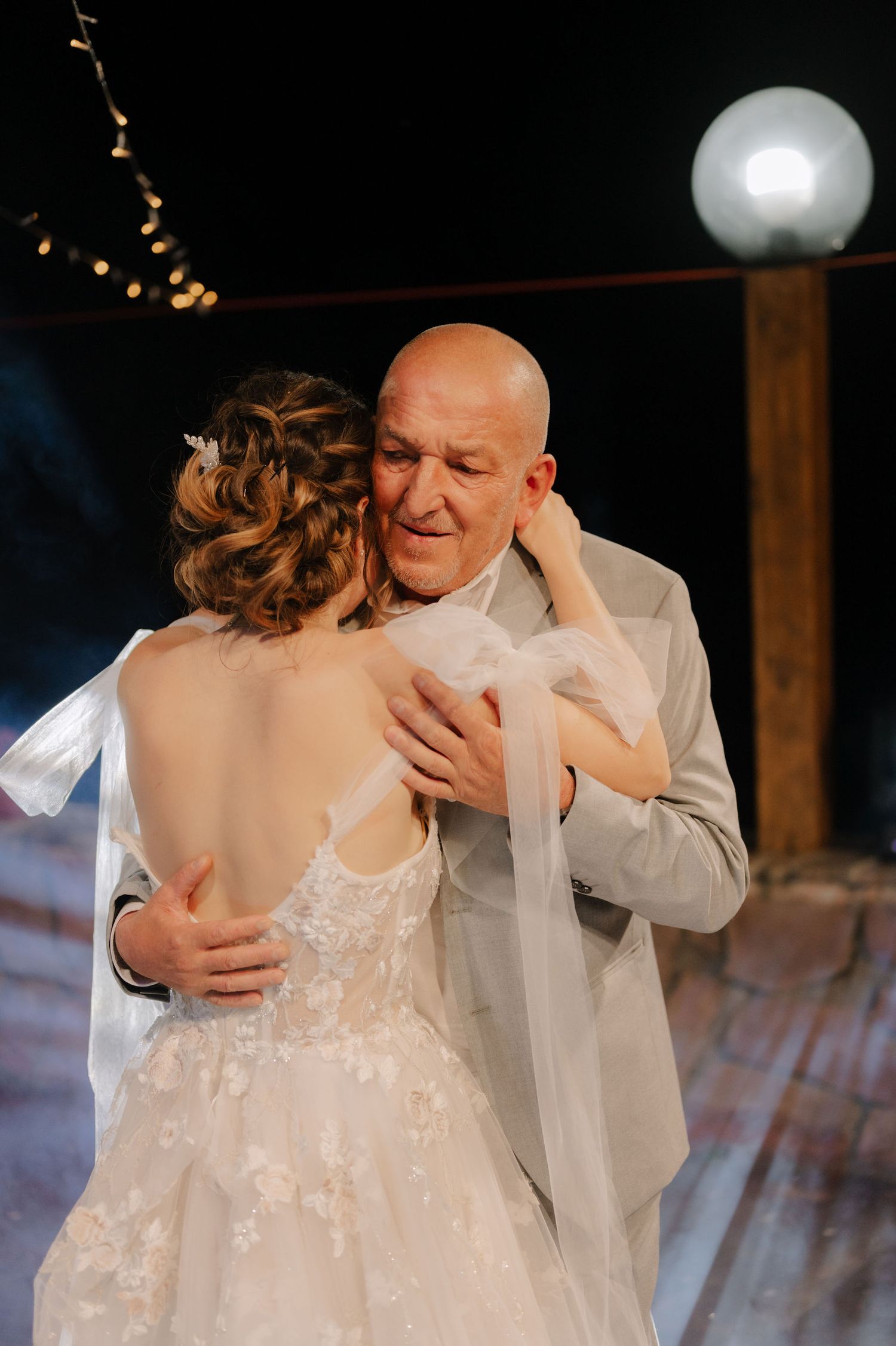 An emotional father-daughter dance captured during a wedding reception with string lights overhead.