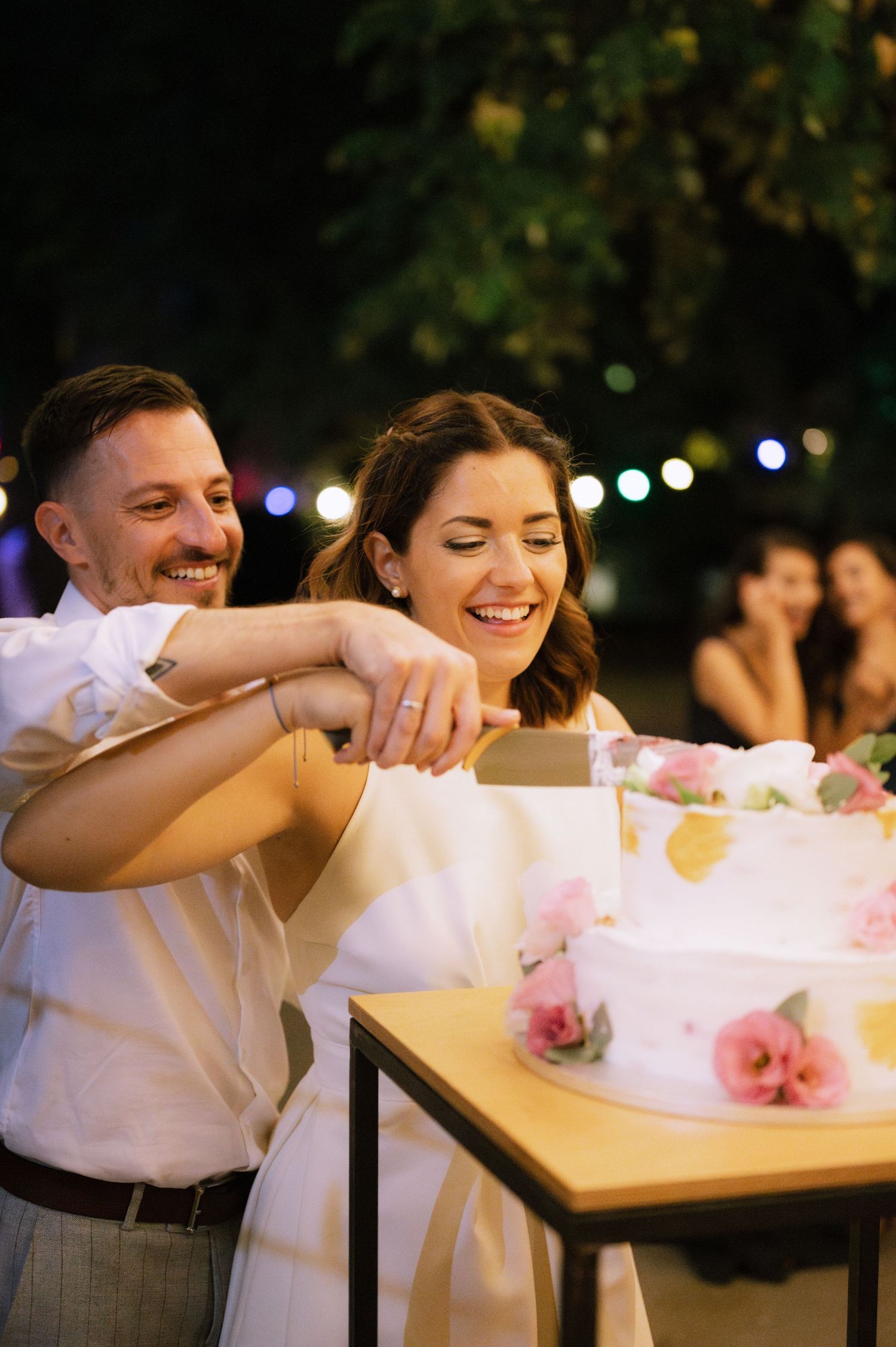 Couple sharing a joyful moment together while cutting their wedding cake at an outdoor evening reception.