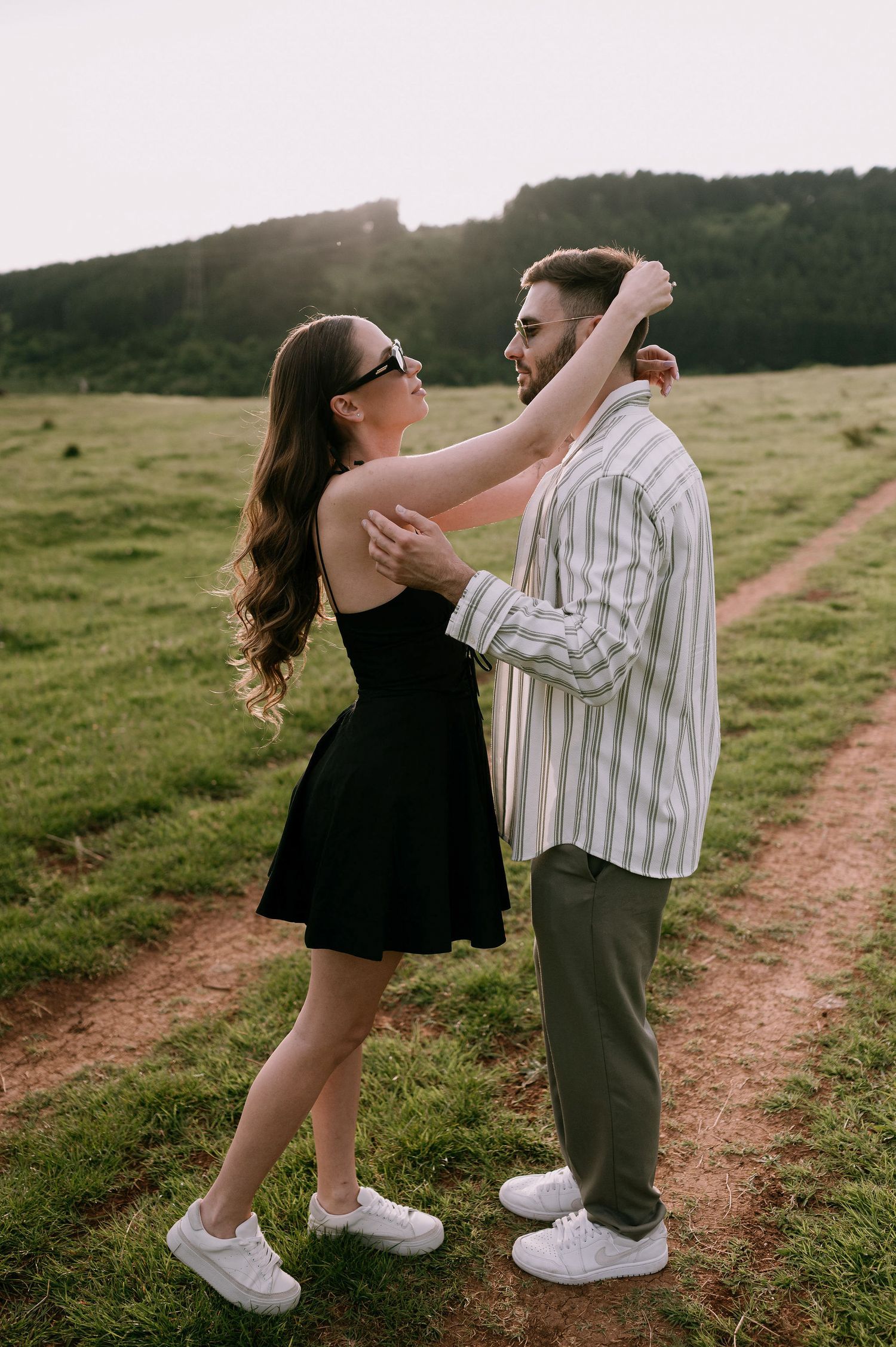 A couple dances together on a dirt path in a grassy field during golden hour.