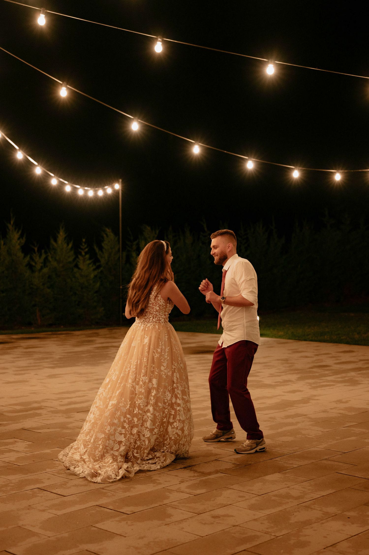 A couple dances together on an outdoor patio under romantic string lights during an evening celebration.