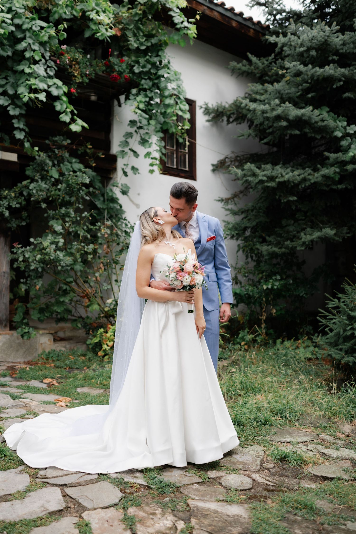 A romantic wedding couple shares intimate moments in a garden setting with stone pathway and lush greenery.