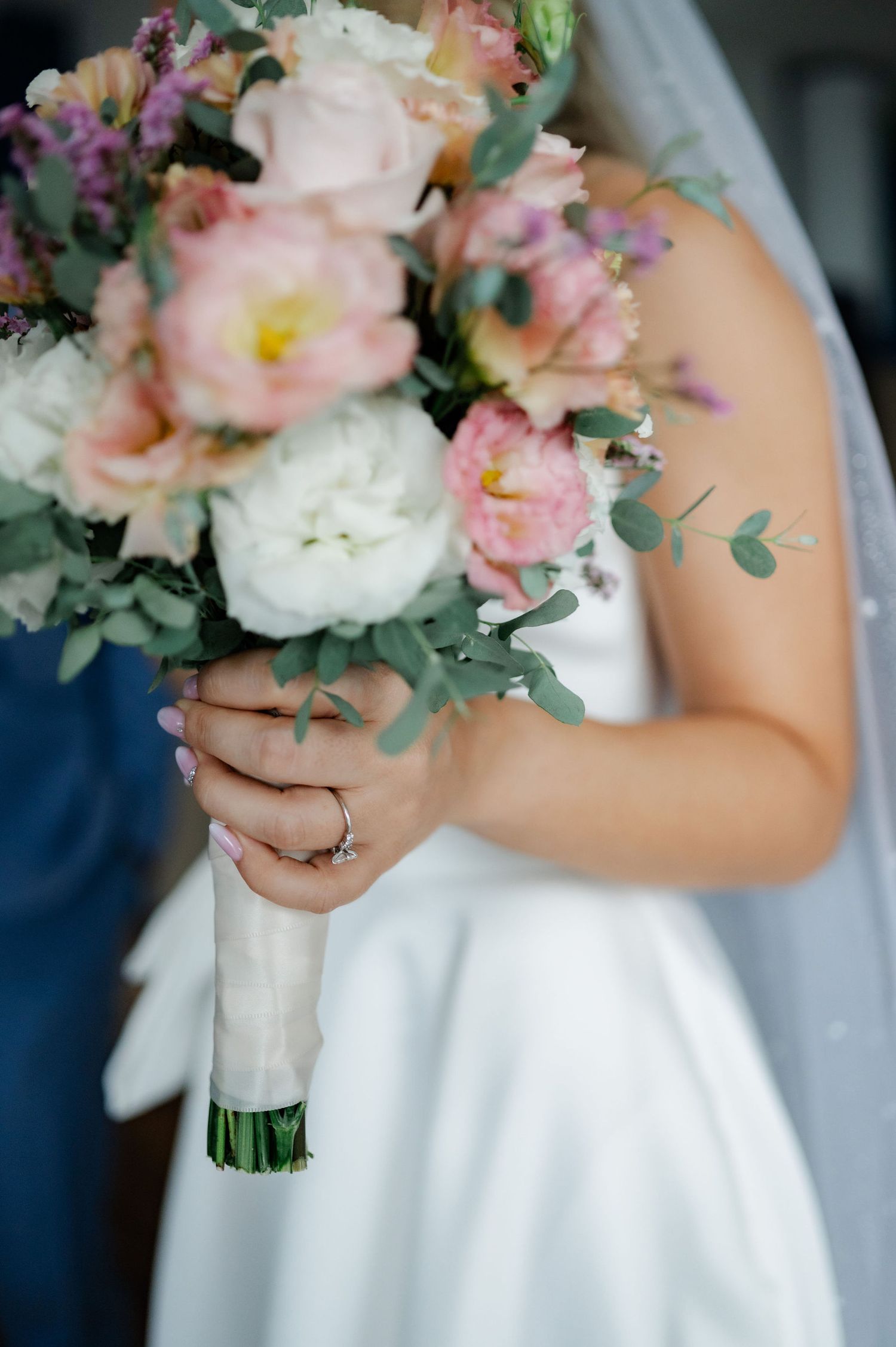 Elegant bridal bouquet featuring soft pink and white flowers with eucalyptus greenery against a white wedding dress.