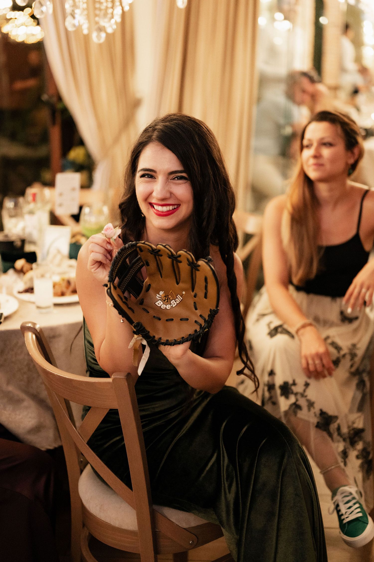 Woman in black dress smiles and laughs during elegant wedding reception with soft lighting and curtains.