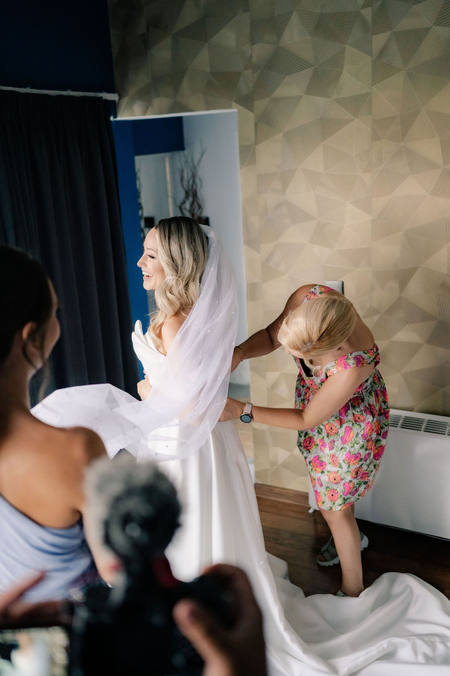 A bride in a white wedding dress gets ready with help from others in a hotel room before the ceremony.