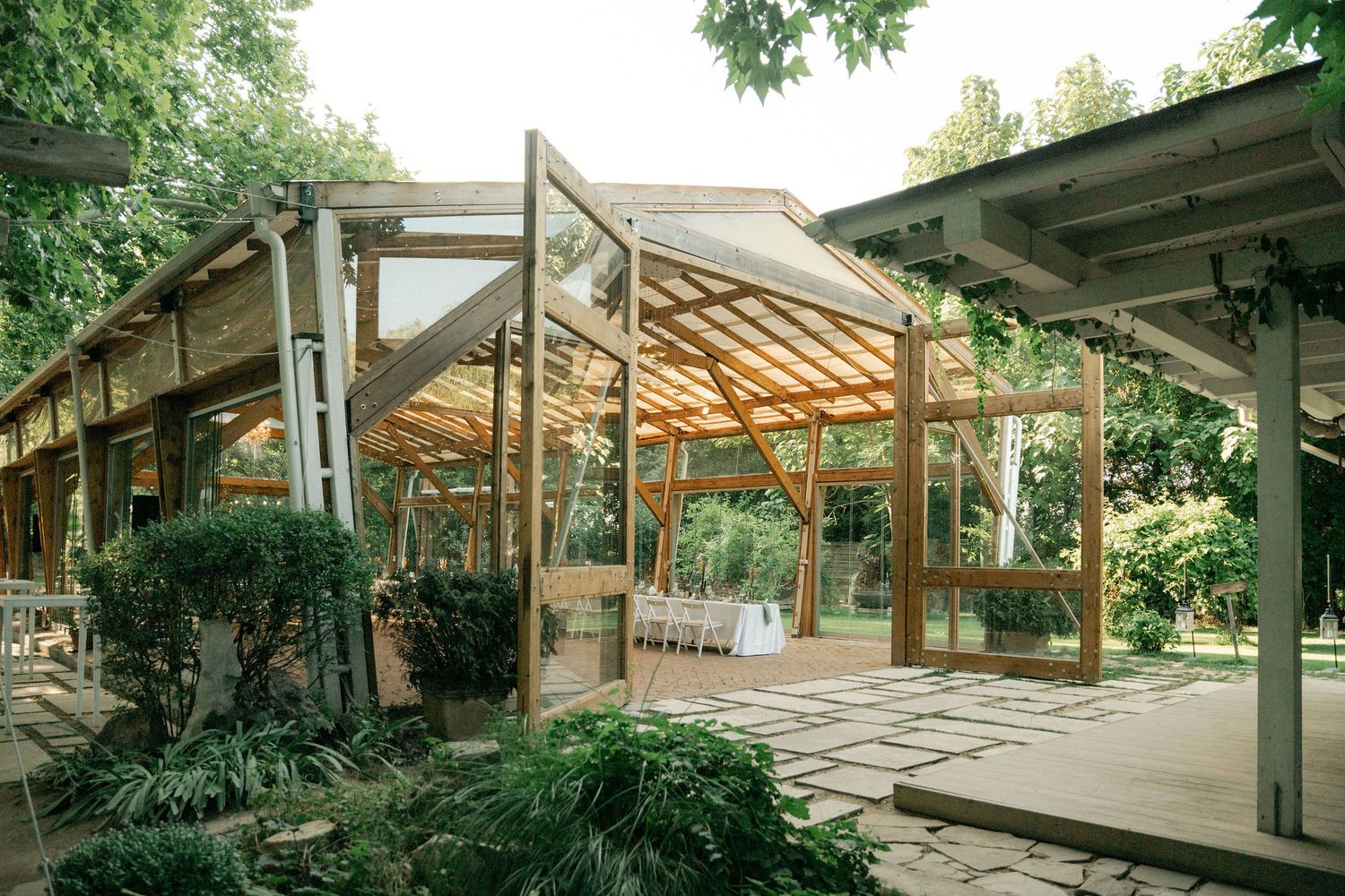 Panoramic view of a modernist home with floor-to-ceiling windows and exposed wooden beams set among lush greenery.