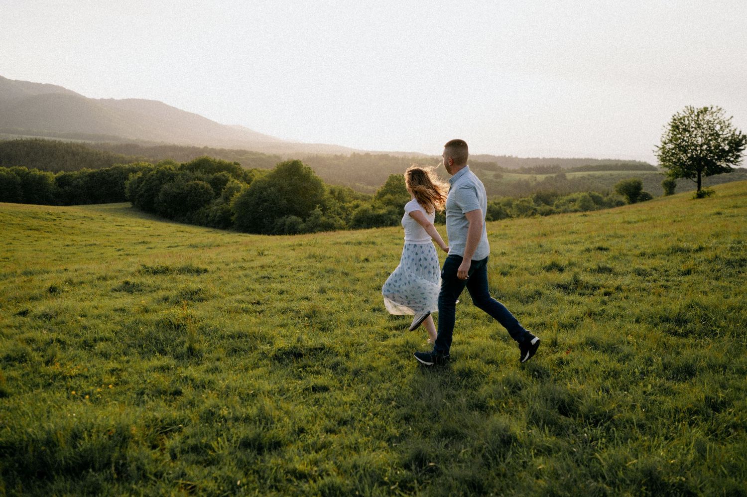 A couple dances together in a scenic mountain meadow during golden hour.