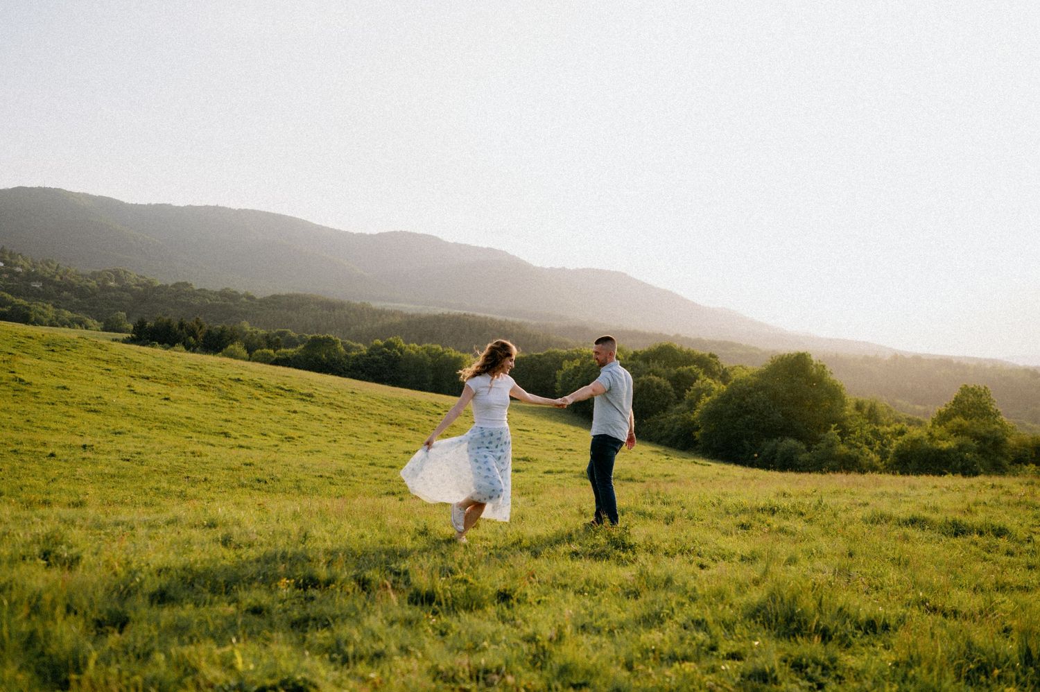 Two figures dance together on a grassy hillside during golden hour.