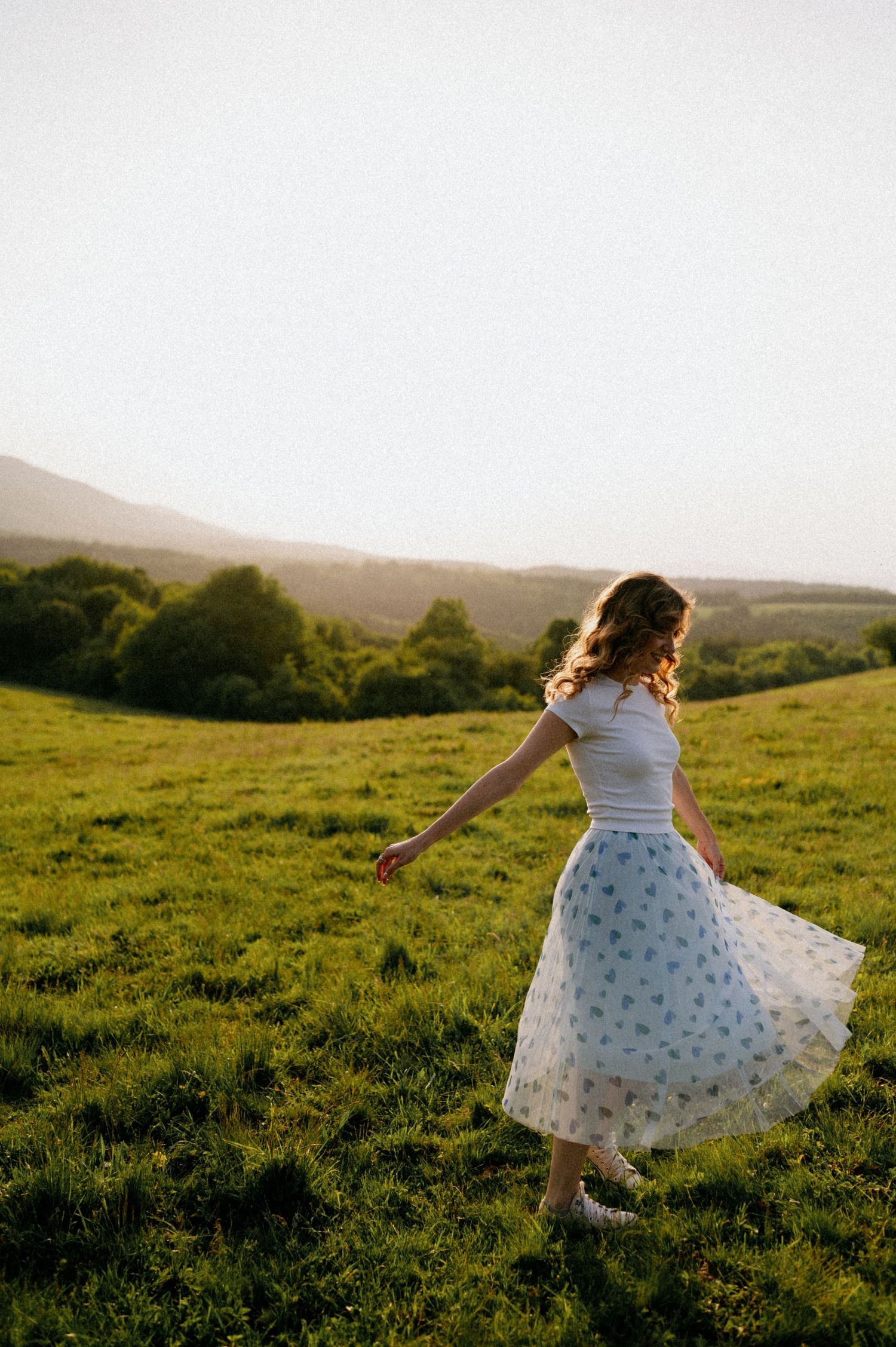Person in floral dress twirling joyfully in a green meadow during golden hour.