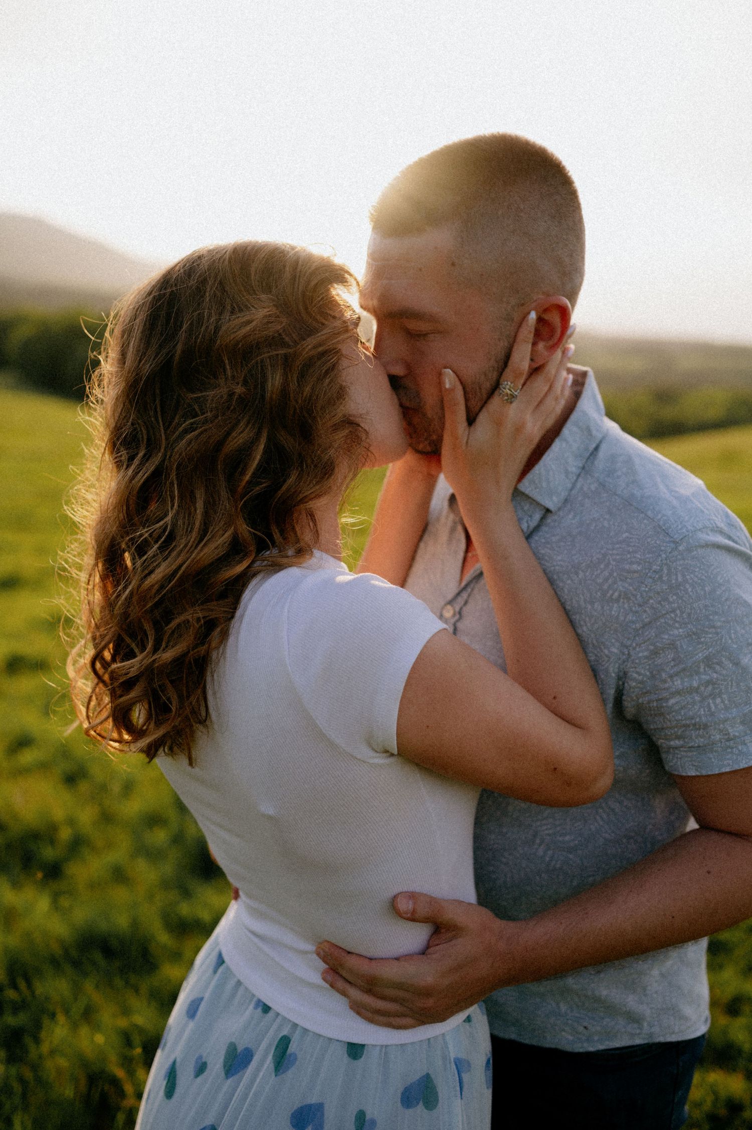 Two people share a tender moment in a grassy field during golden hour.