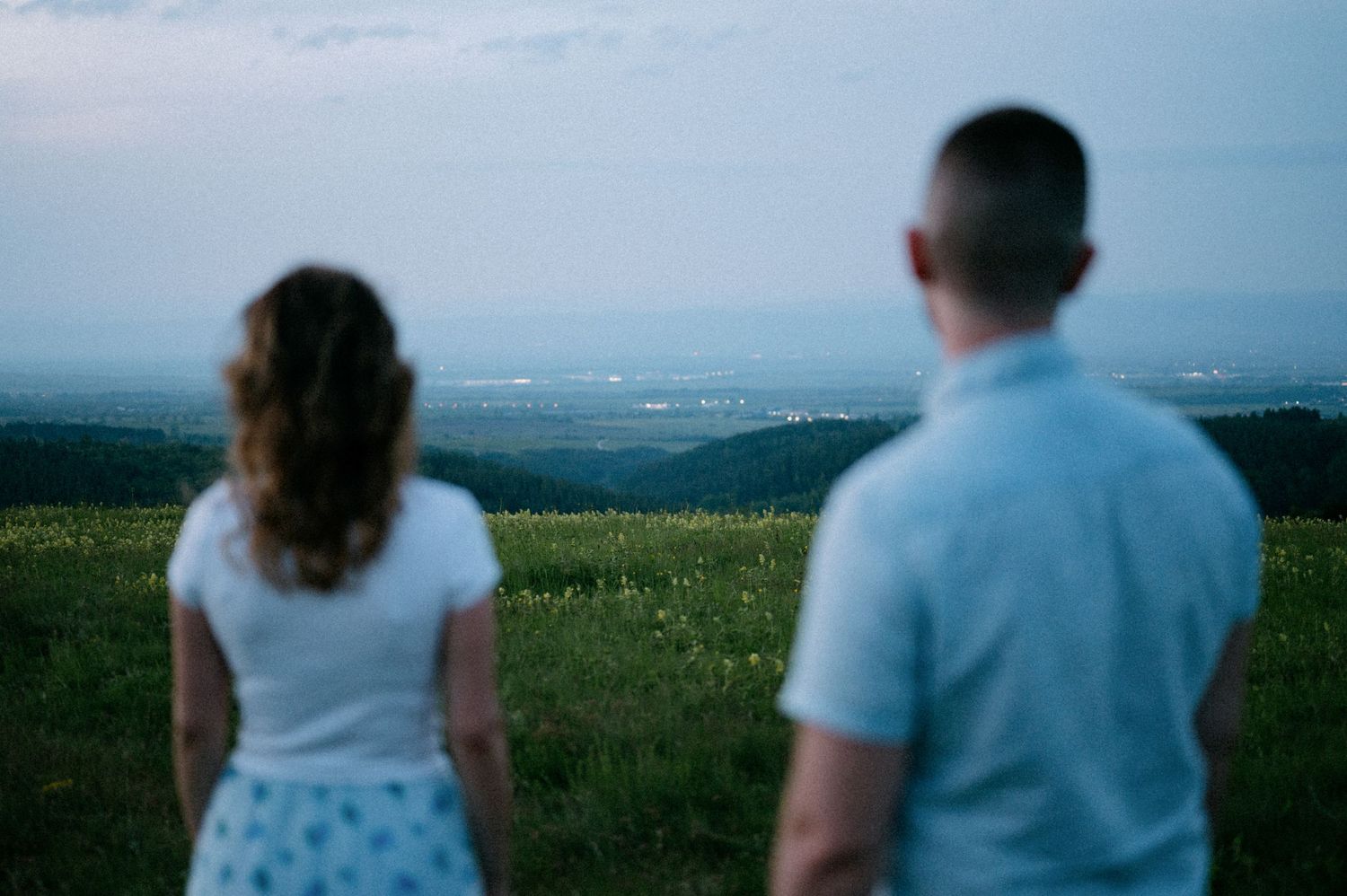People enjoying a scenic overlook with mountains and fields in the distance.