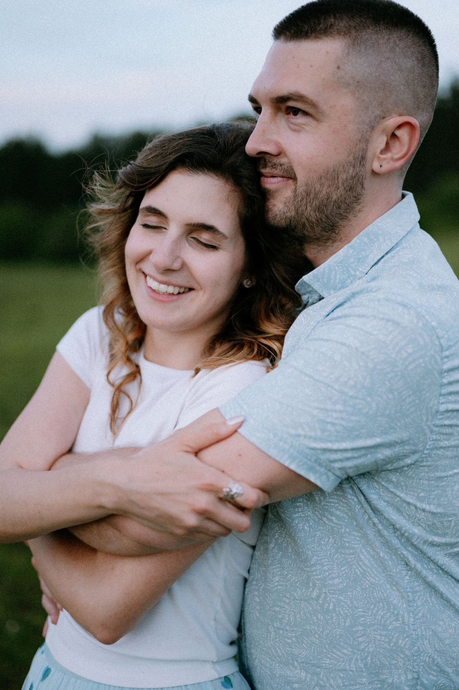A tender moment captured between two people hugging and smiling in an outdoor setting.
