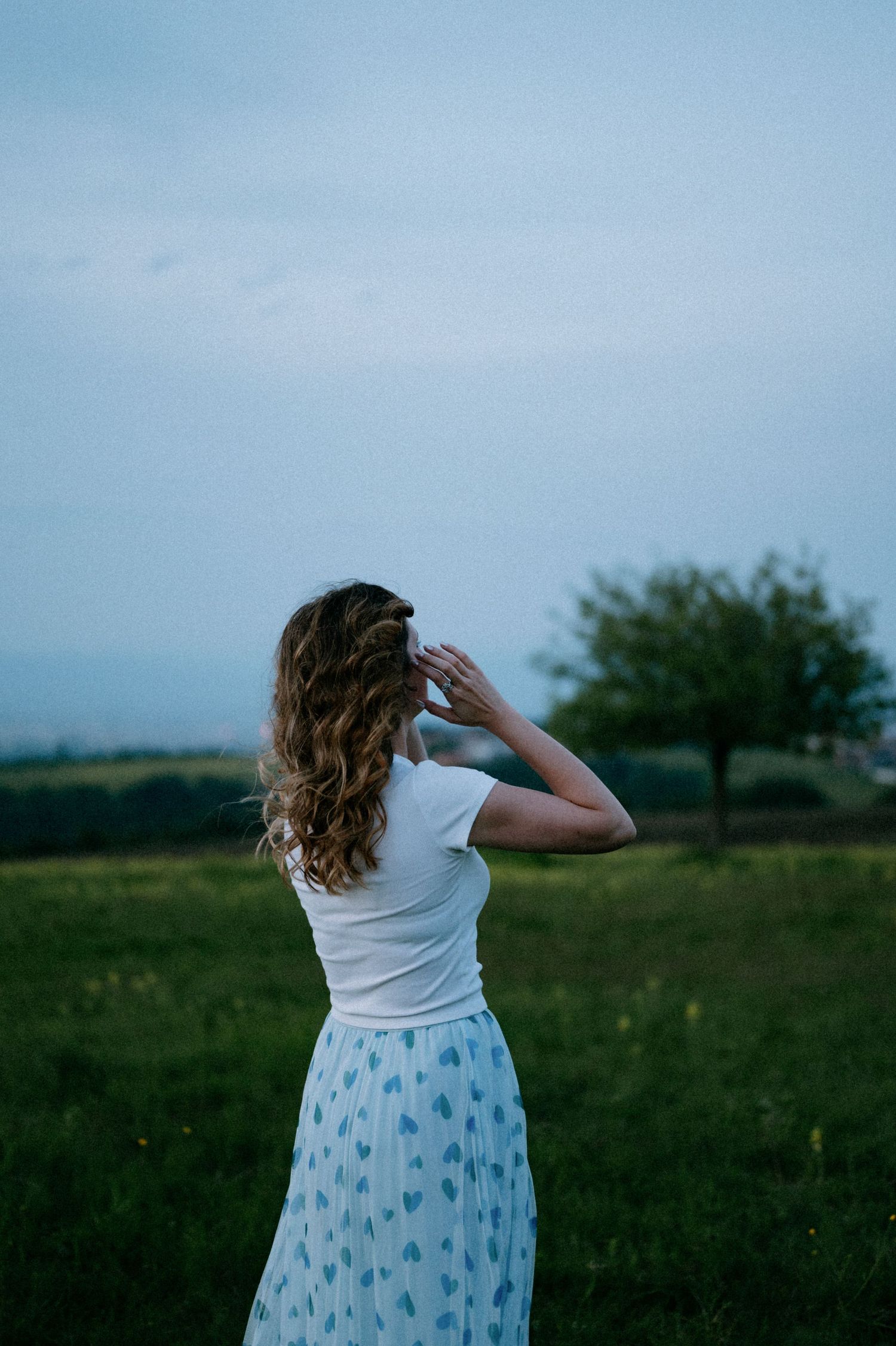 A person in a white top and patterned skirt looks out over a scenic landscape.