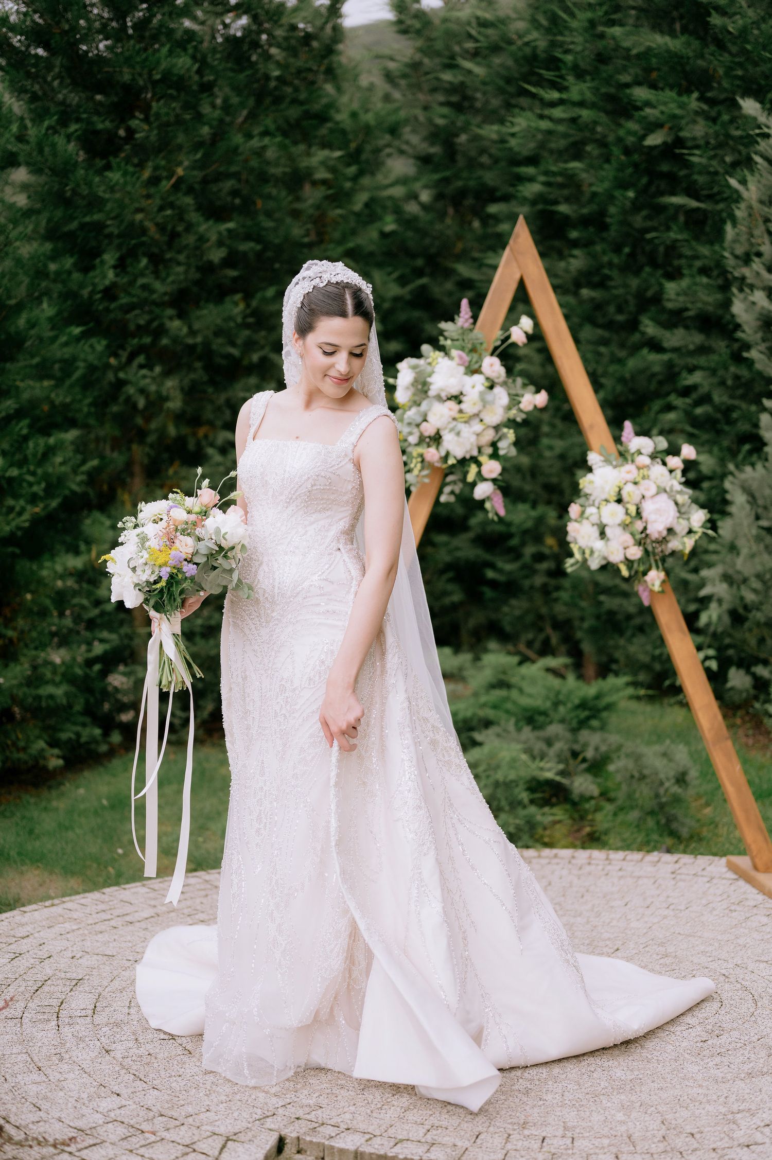 Elegant bridal portrait in a white lace gown against a wooden triangle arch decorated with white florals.