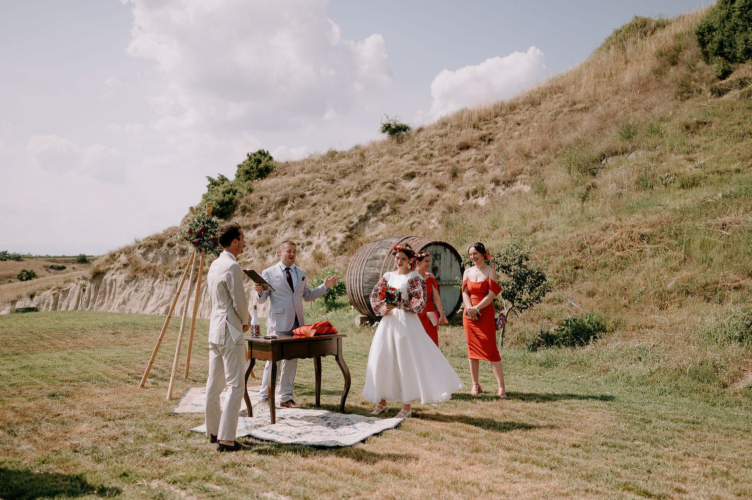 Outdoor wedding ceremony setup on hillside with vintage furniture and boho decorations.