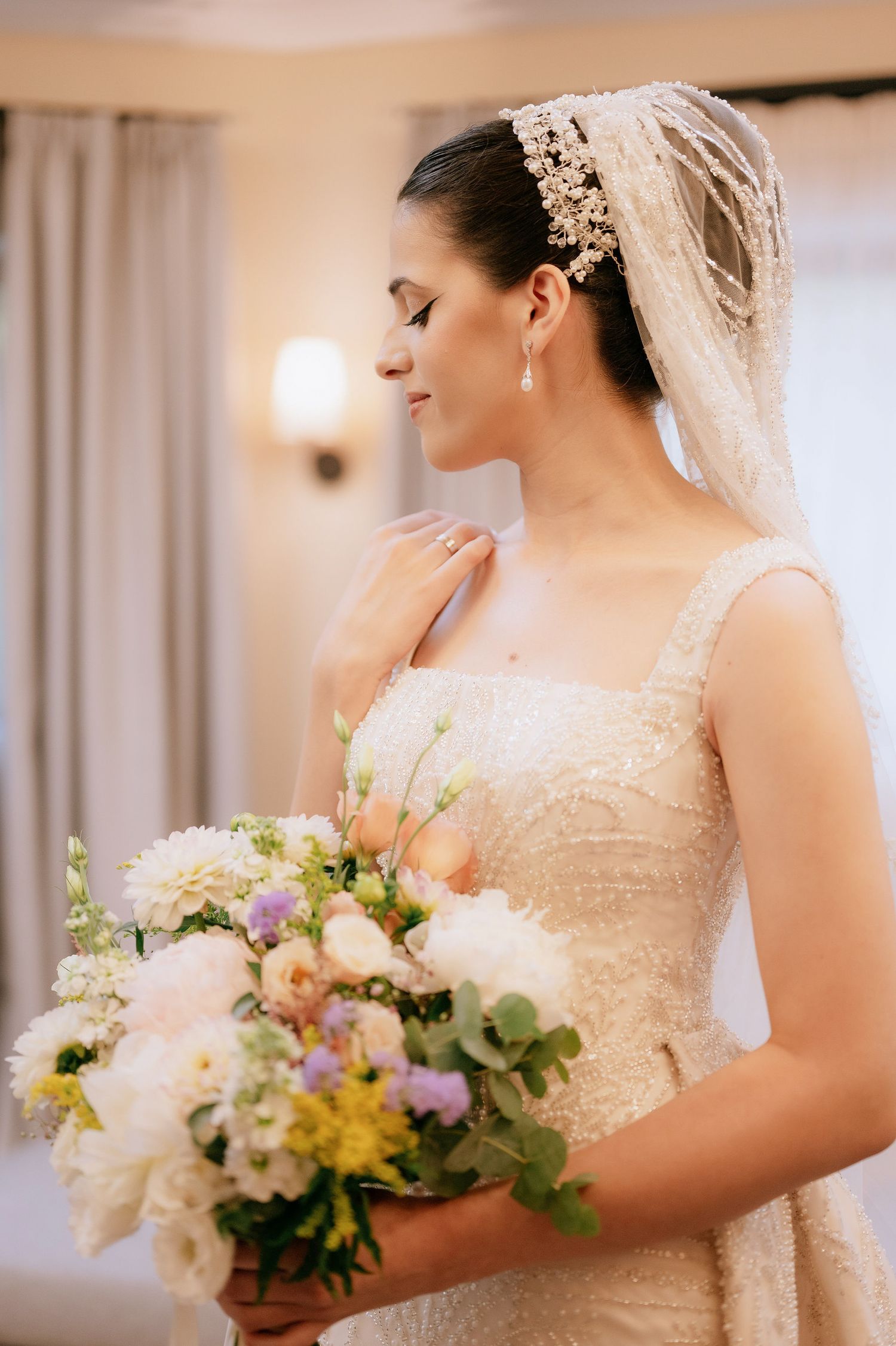 Classic bridal portrait showing detailed veil and mixed flower bouquet in soft lighting.