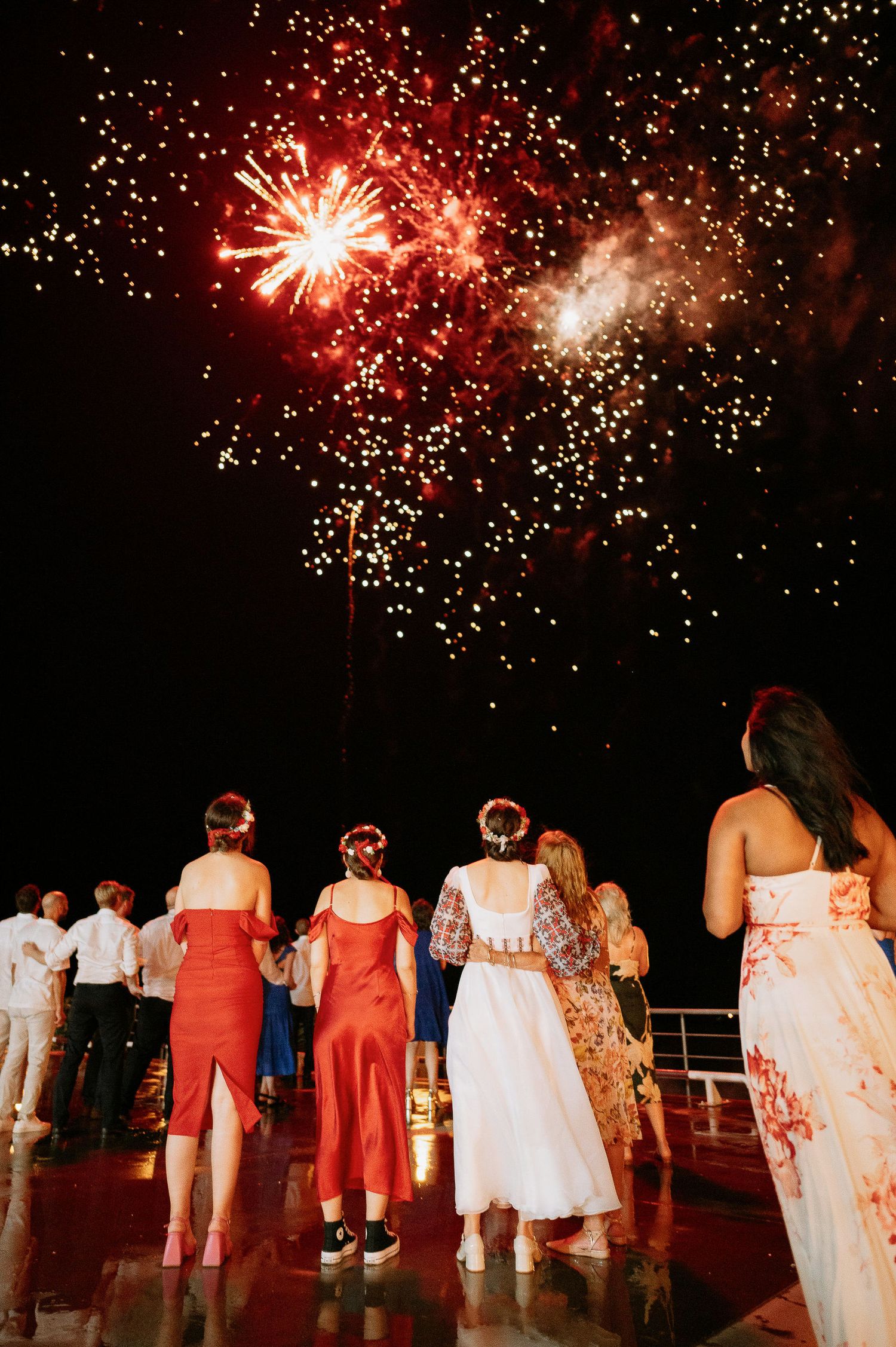 Silhouetted wedding guests watch a spectacular red fireworks display in the night sky.