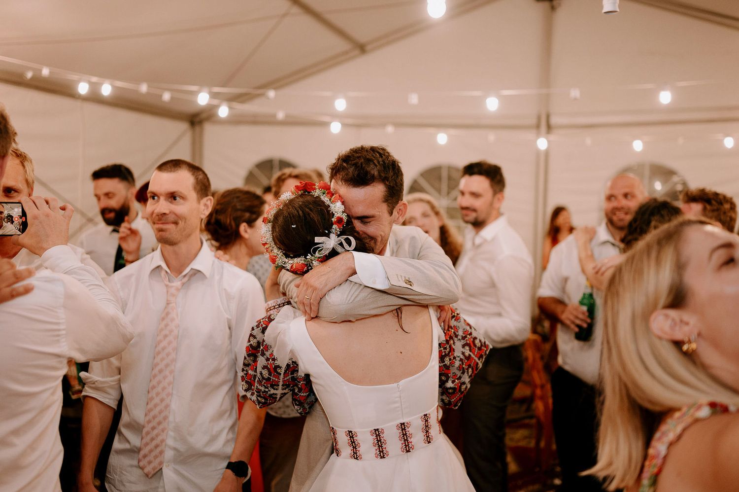 Lively dance floor at wedding reception with guests celebrating under tent lighting.
