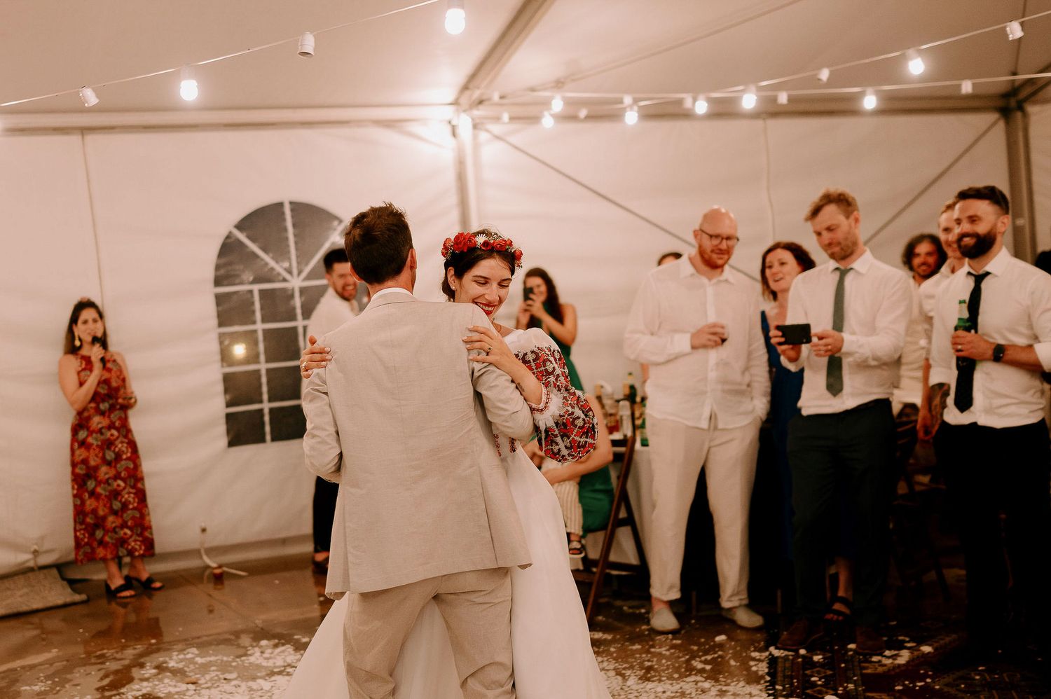 Wedding celebration in full swing with guests dancing under tent lighting.