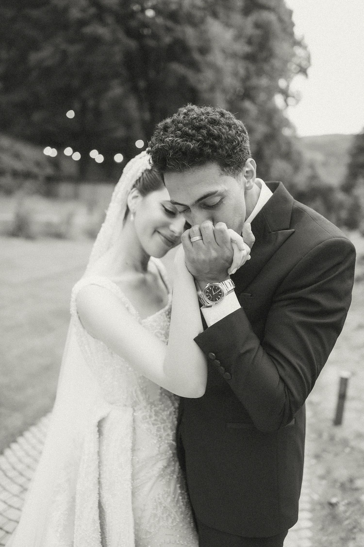 An emotional black and white wedding portrait captured outdoors with bokeh lights.