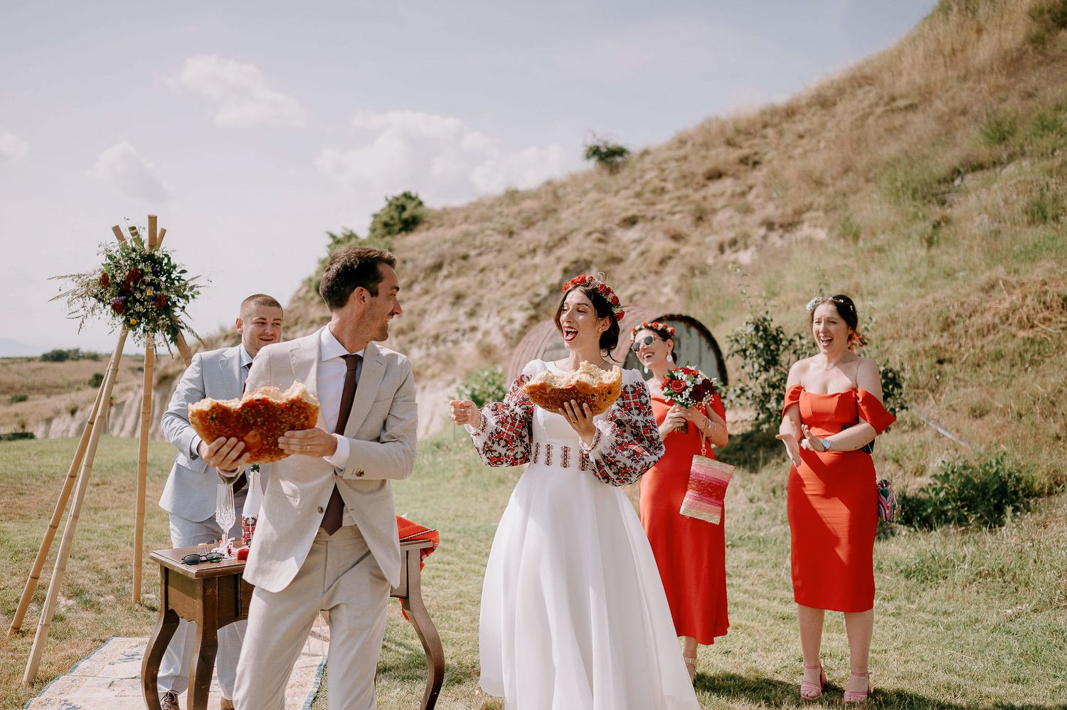 Wedding ceremony setup on a grassy hillside with bright coral and white decor.