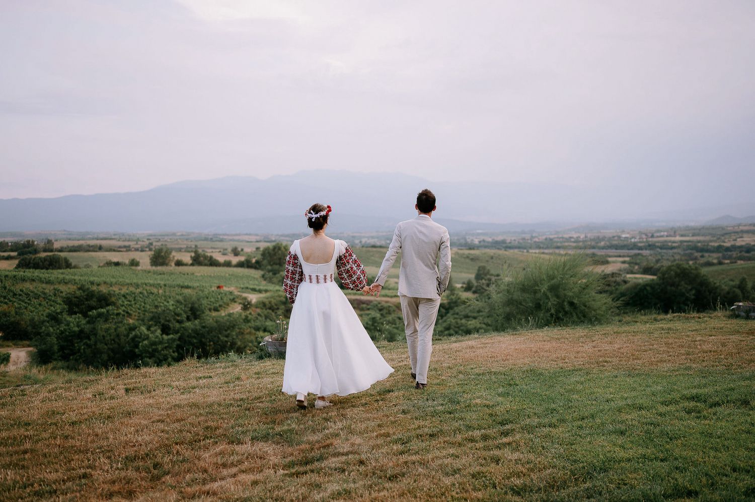 Bride and groom walking hand in hand through rolling hills at sunset.