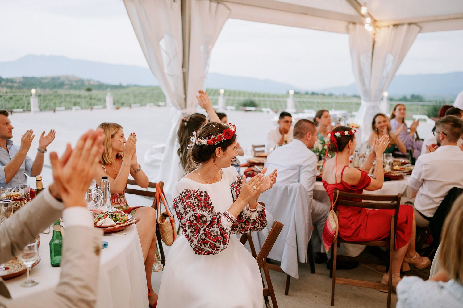 Wedding celebration with guests raising their hands in joy under a white tent with mountain backdrop.