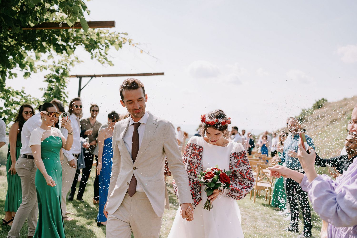 Wedding guests celebrate as the couple walks down a hillside path after their ceremony.