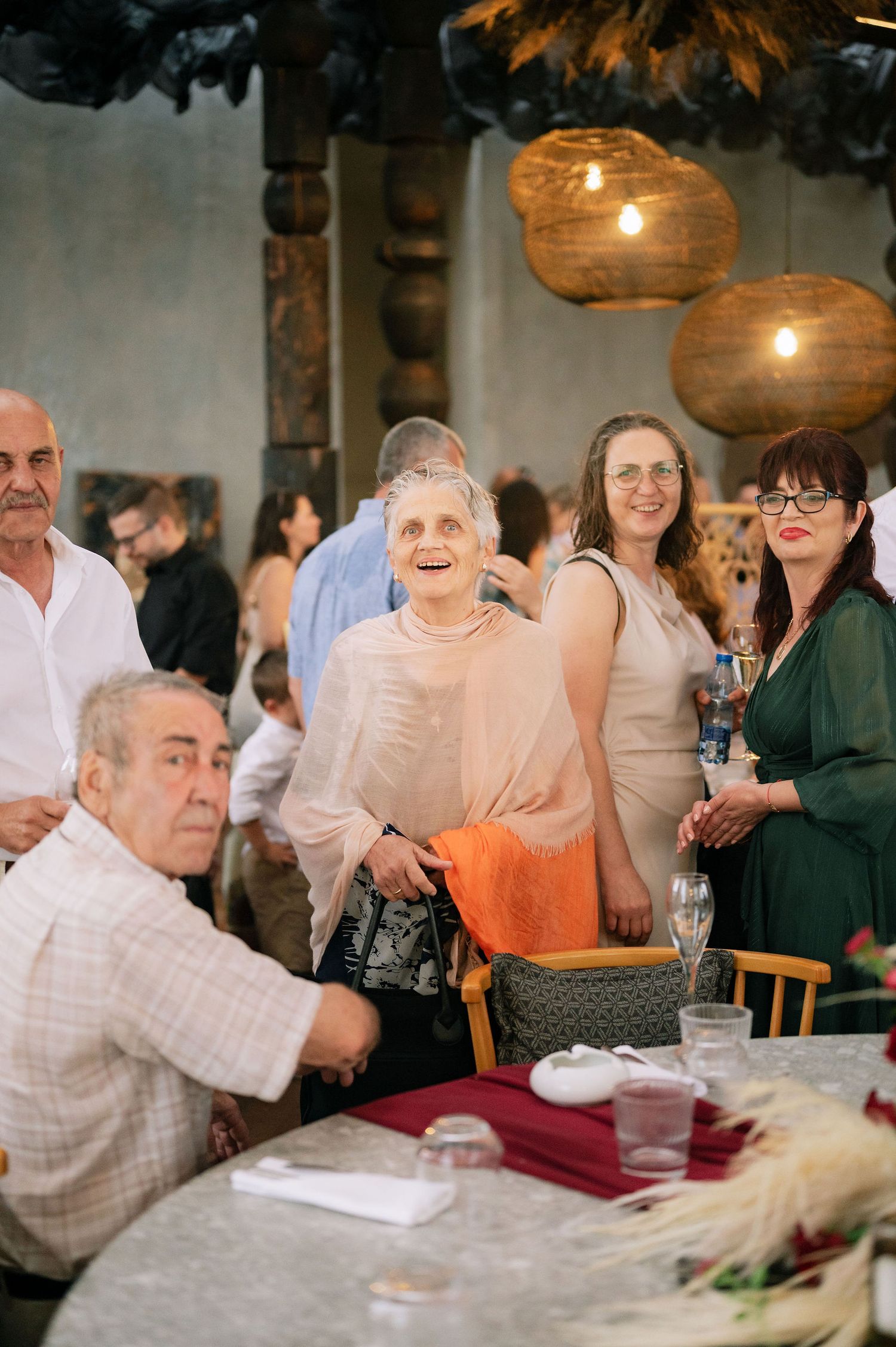 Guests gather around decorated tables under warm pendant lighting at an indoor celebration.