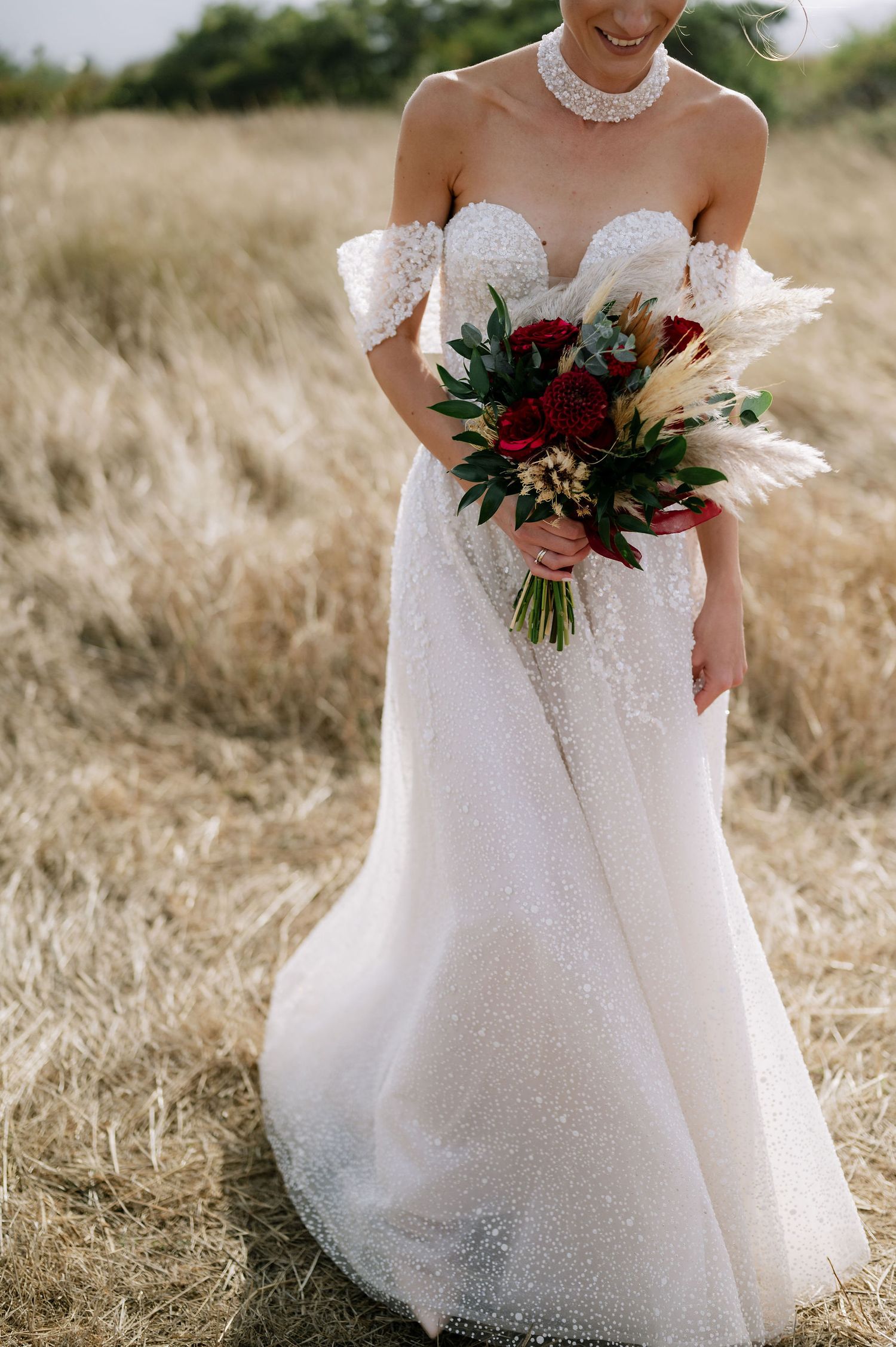 Close-up of a sparkling white wedding dress with a red and white bouquet.