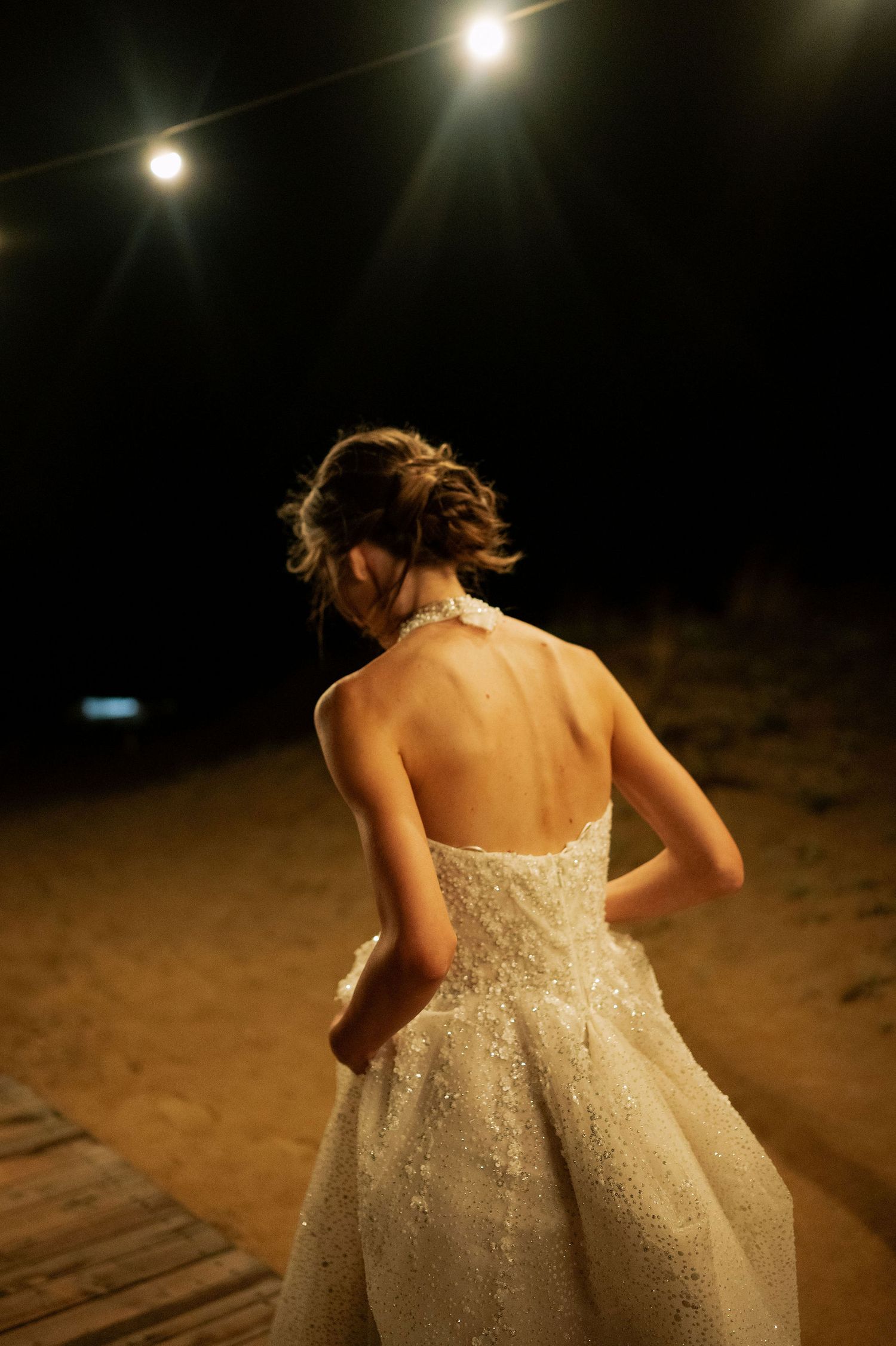 Back view of a sparkling white wedding dress under outdoor string lights at night.