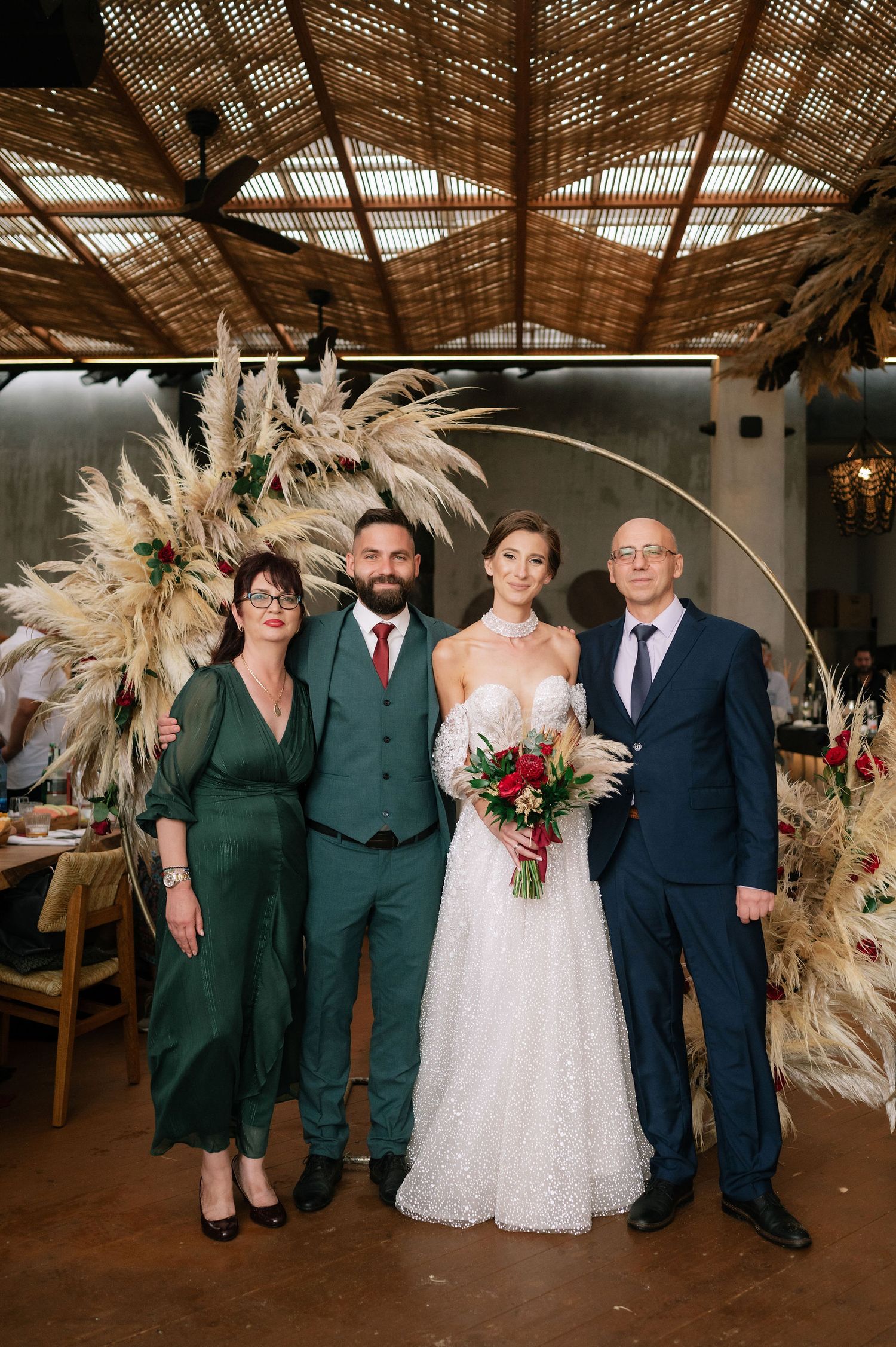 Wedding group photo in rustic venue with pampas grass arrangements and natural lighting.