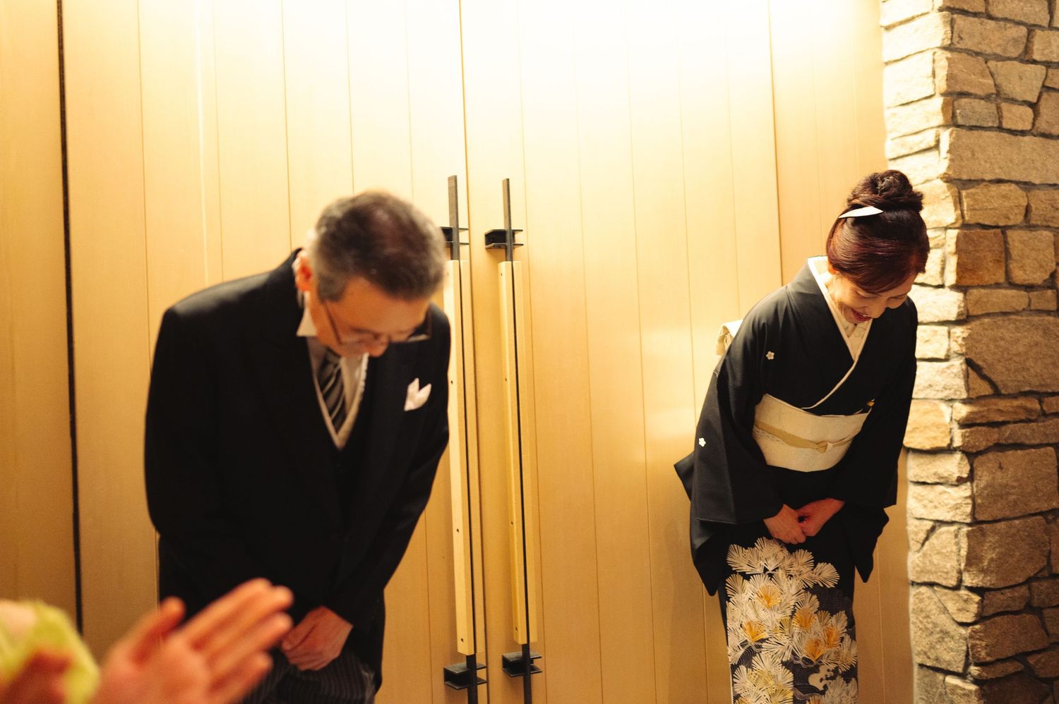 Wedding guests in formal attire gather in an elegant hallway with stone walls and warm lighting.