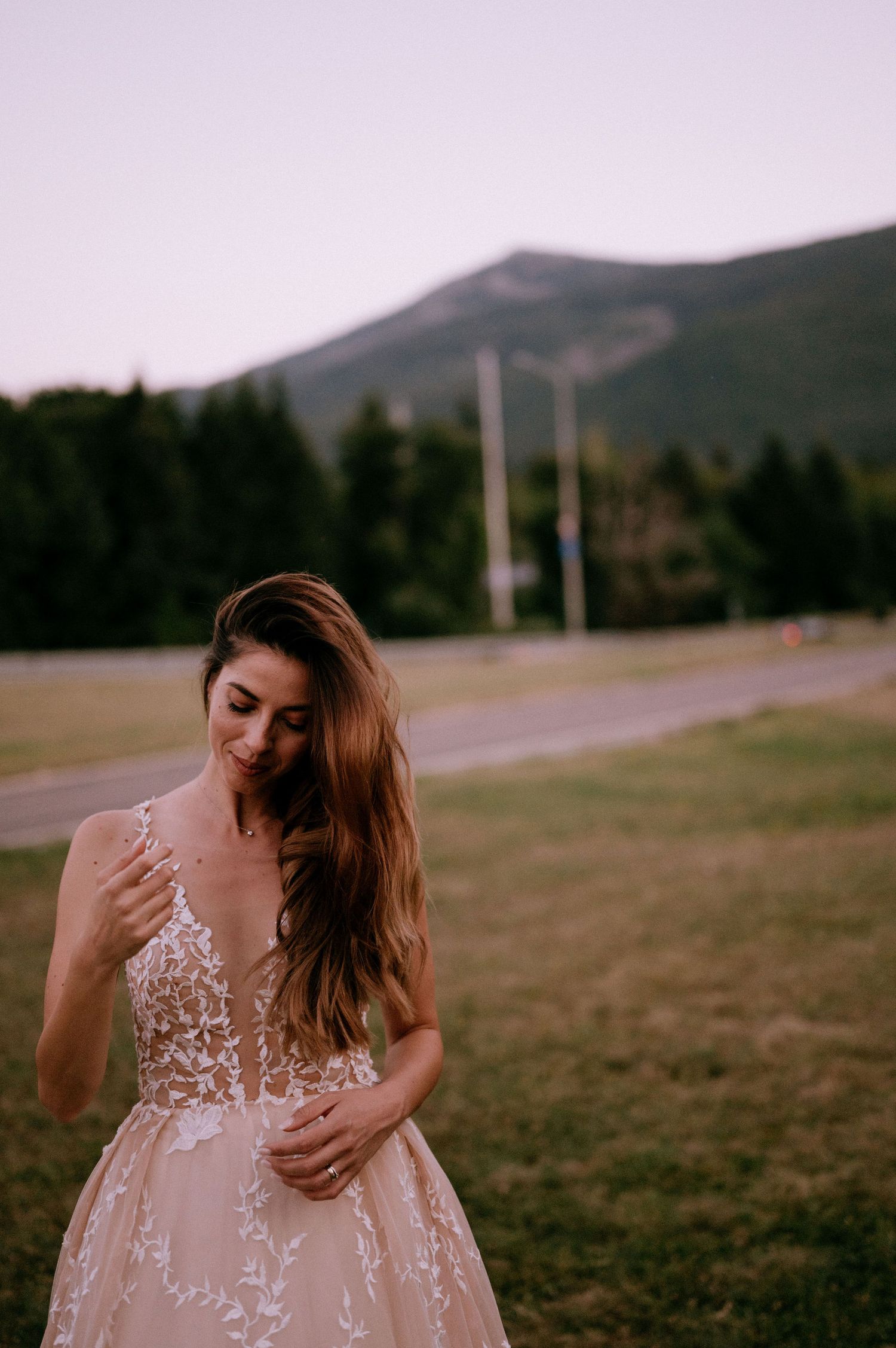 Ethereal bridal portrait in a blush gown with lace details against a mountain landscape at sunset.