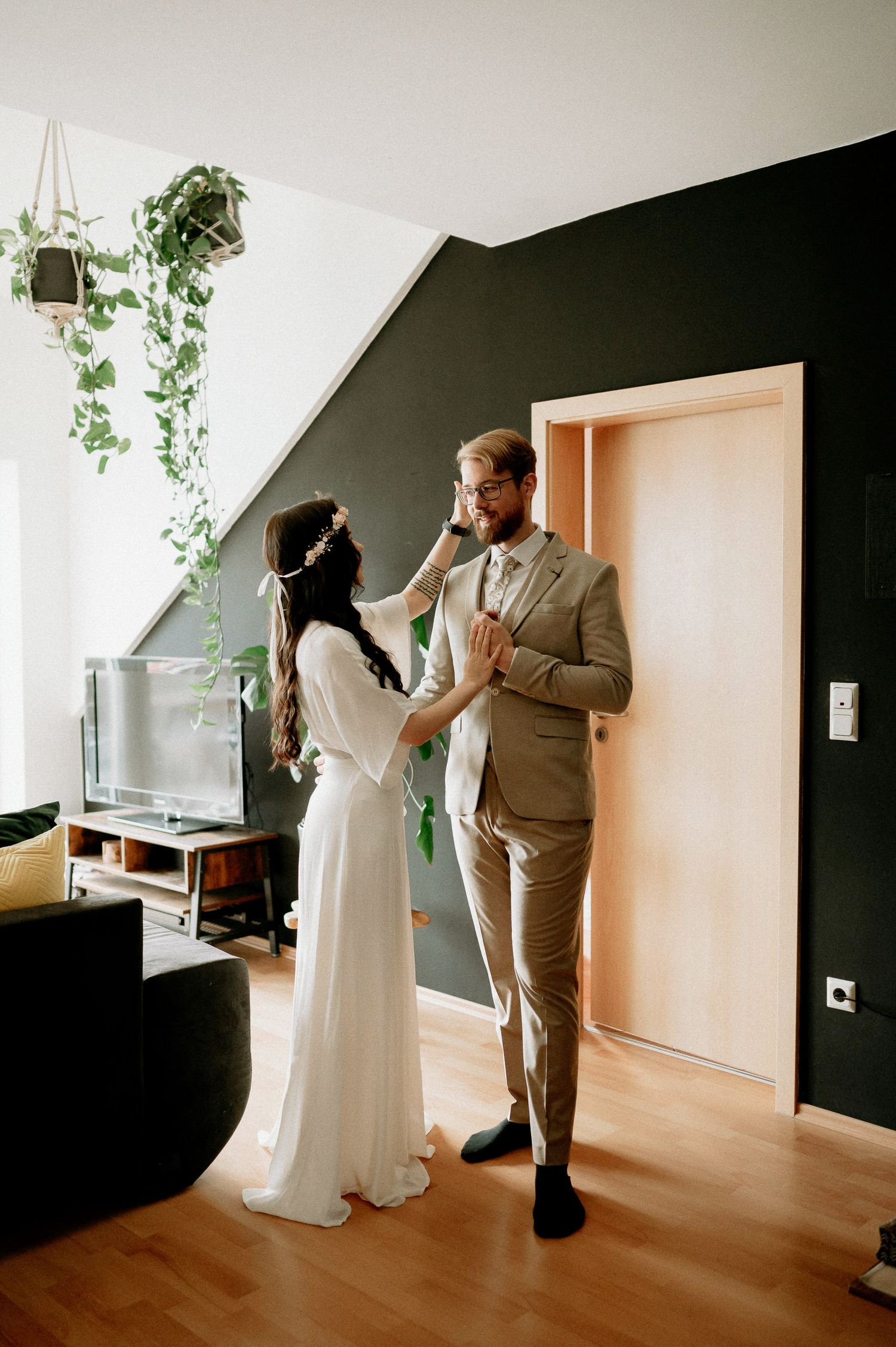 A couple in wedding attire dancing together in a minimalist room with black walls and wooden floors.